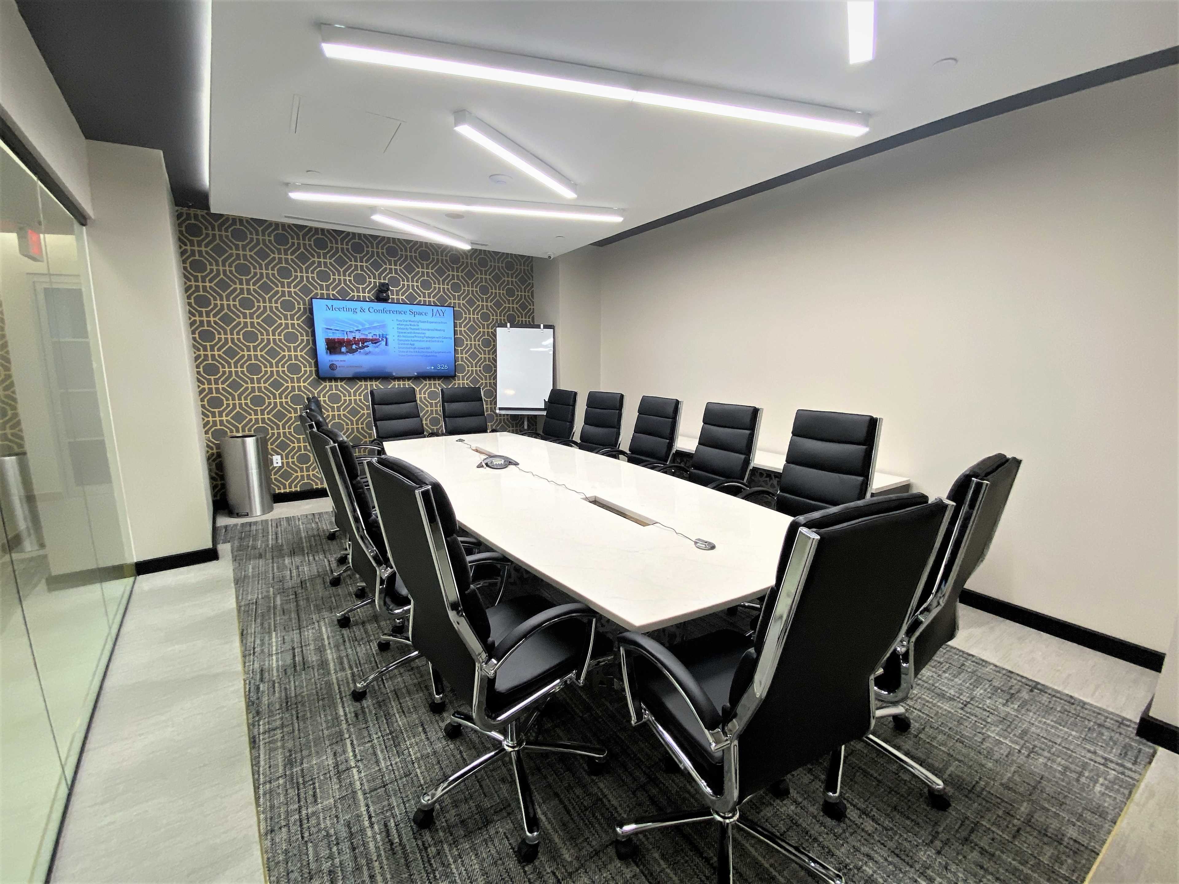 A modern conference room equipped with a long rectangular table, black leather chairs, and a large screen on the wall.