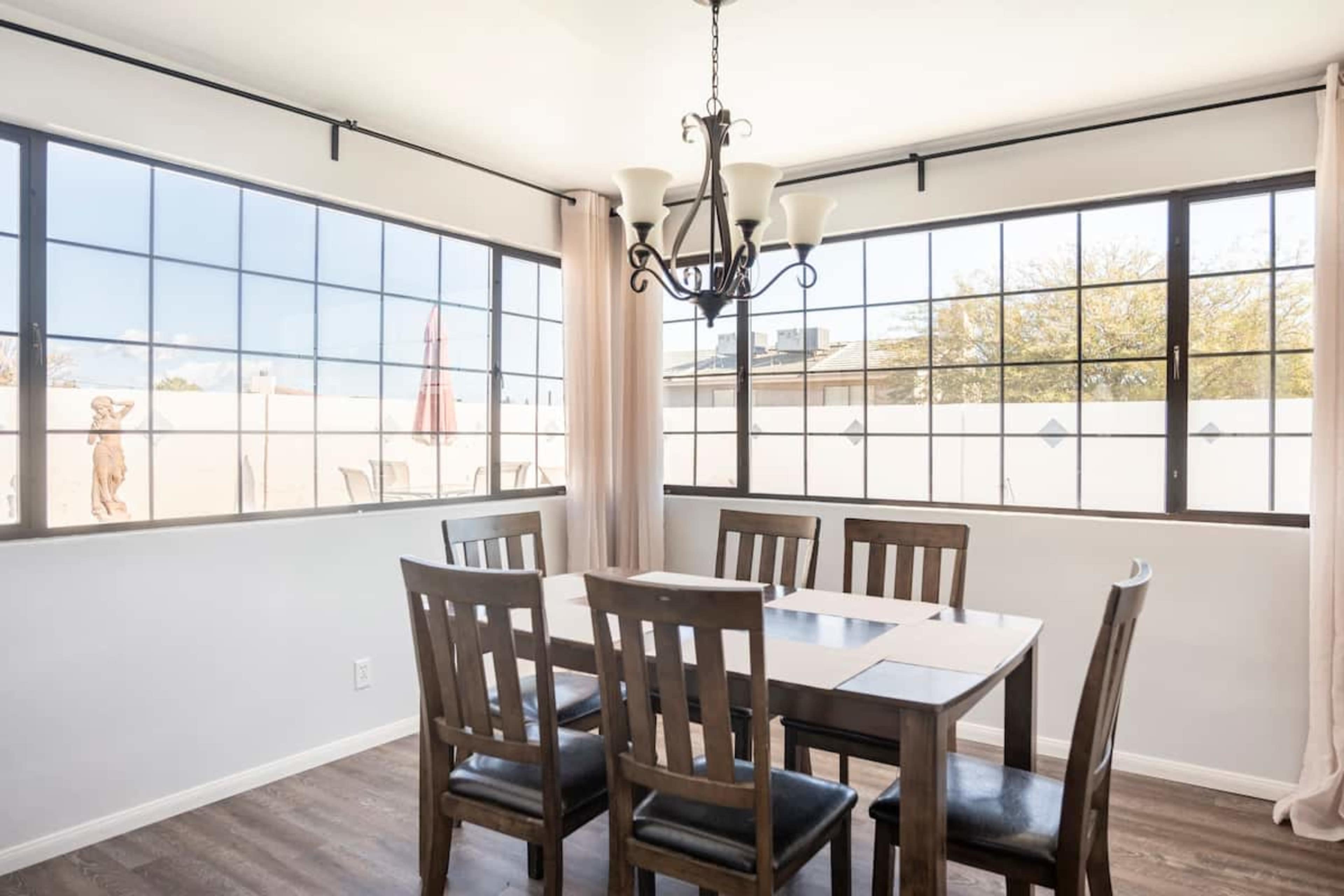 A dining area features a wooden table with four chairs, large windows, and a chandelier.