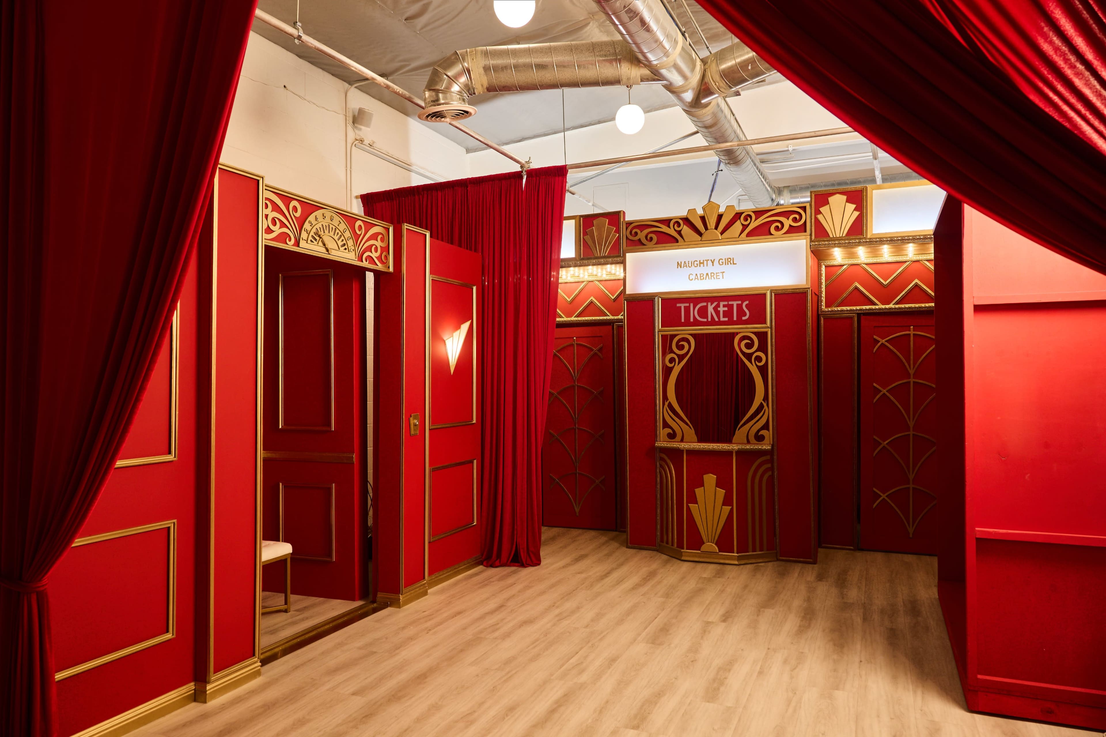 The image shows a vibrant room decorated in red with gold accents, featuring a ticket booth labeled "NIGHT GIRL" and curtains on either side.