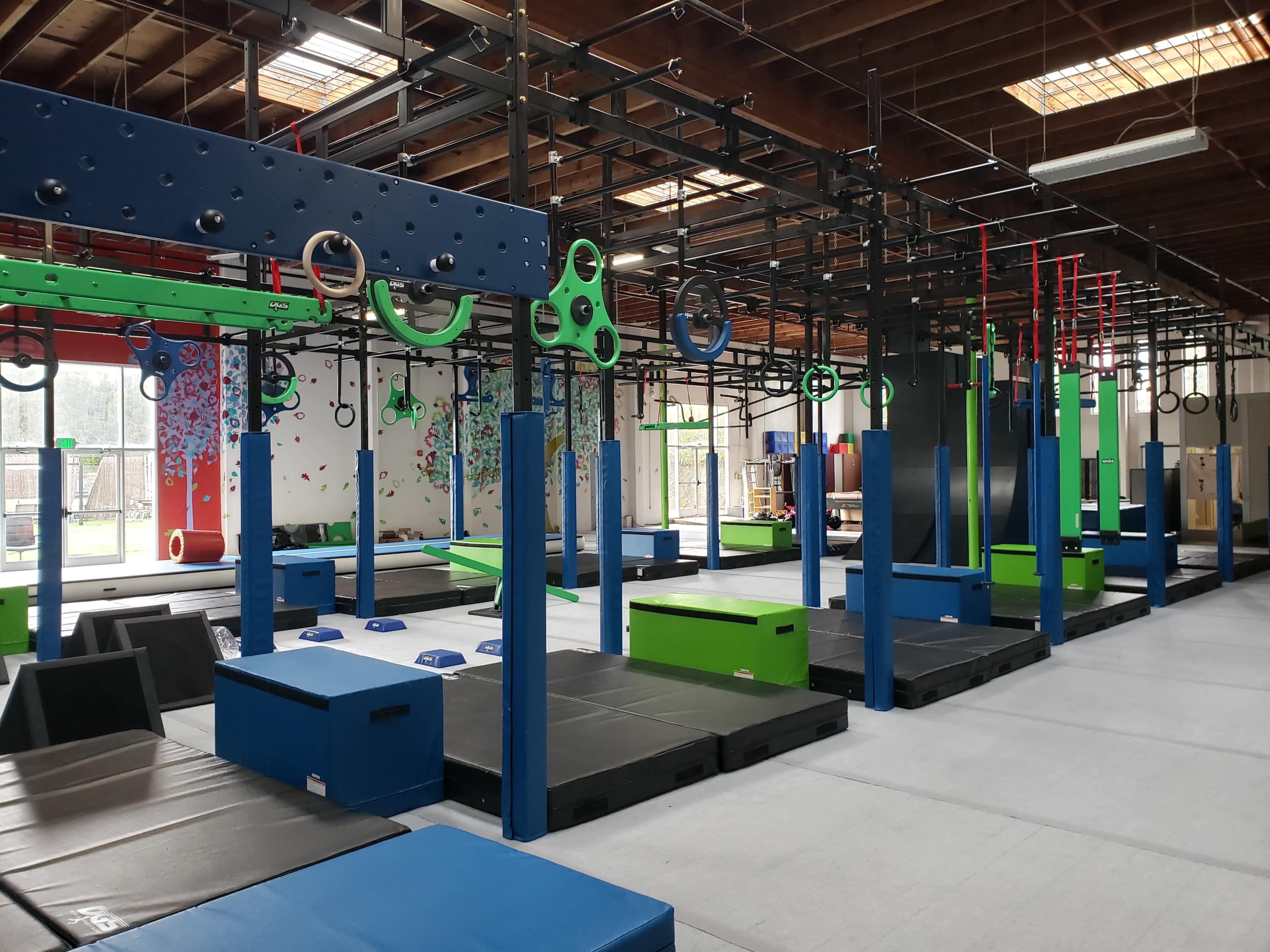 An indoor gym with various training equipment, including climbing structures, mats, and rings, arranged in a spacious facility.