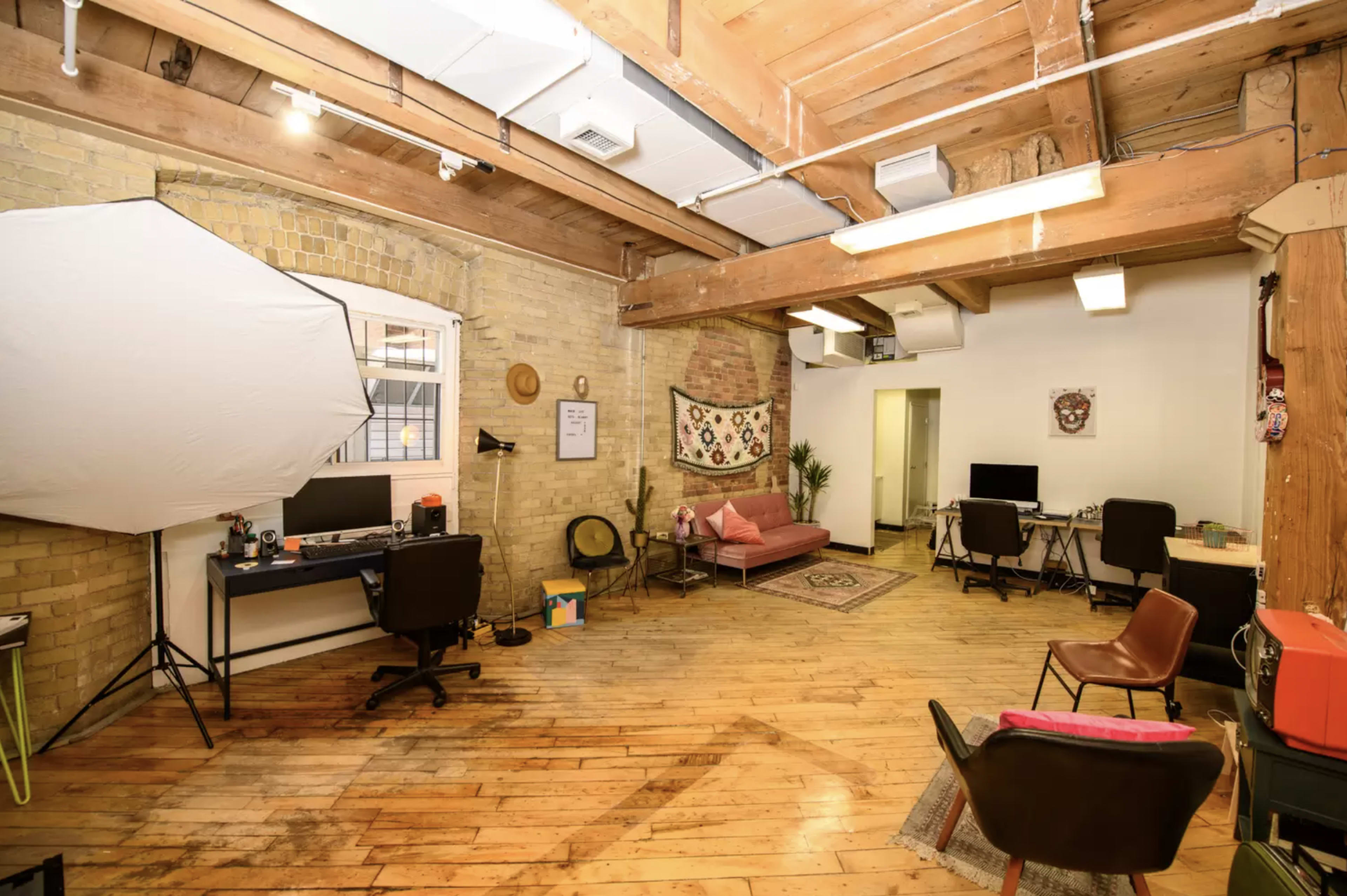A bright, open office space with wooden beams, a mix of workstations, and a seating area featuring a pink couch and decorative elements.