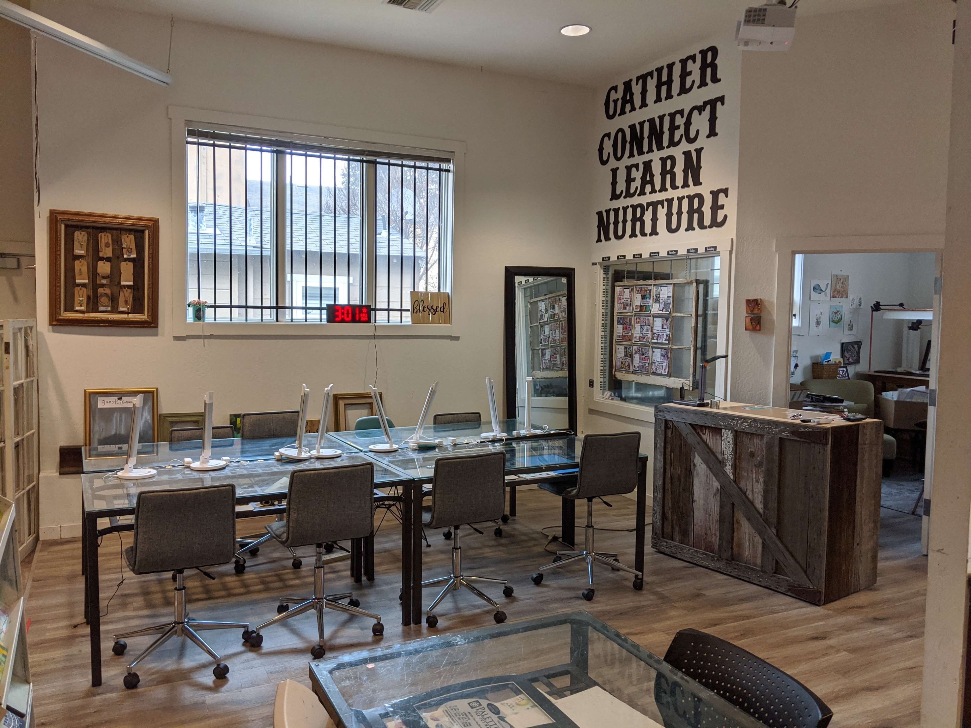 A conference room features a long glass table surrounded by rolling chairs, with inspirational words displayed on the wall and a view of a courtyard through the window.