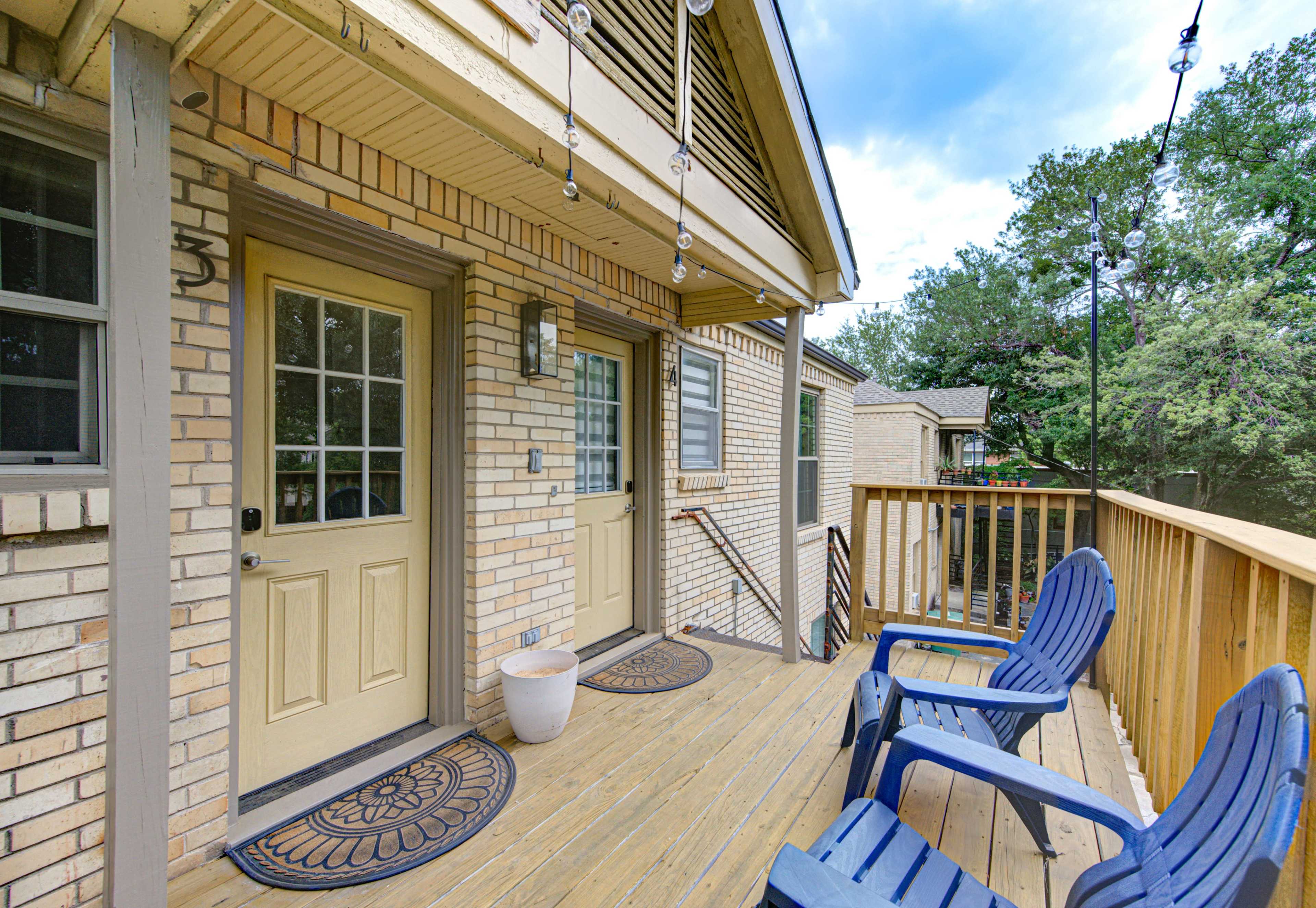 A wooden deck with two blue chairs in front of a brick building featuring two doors.