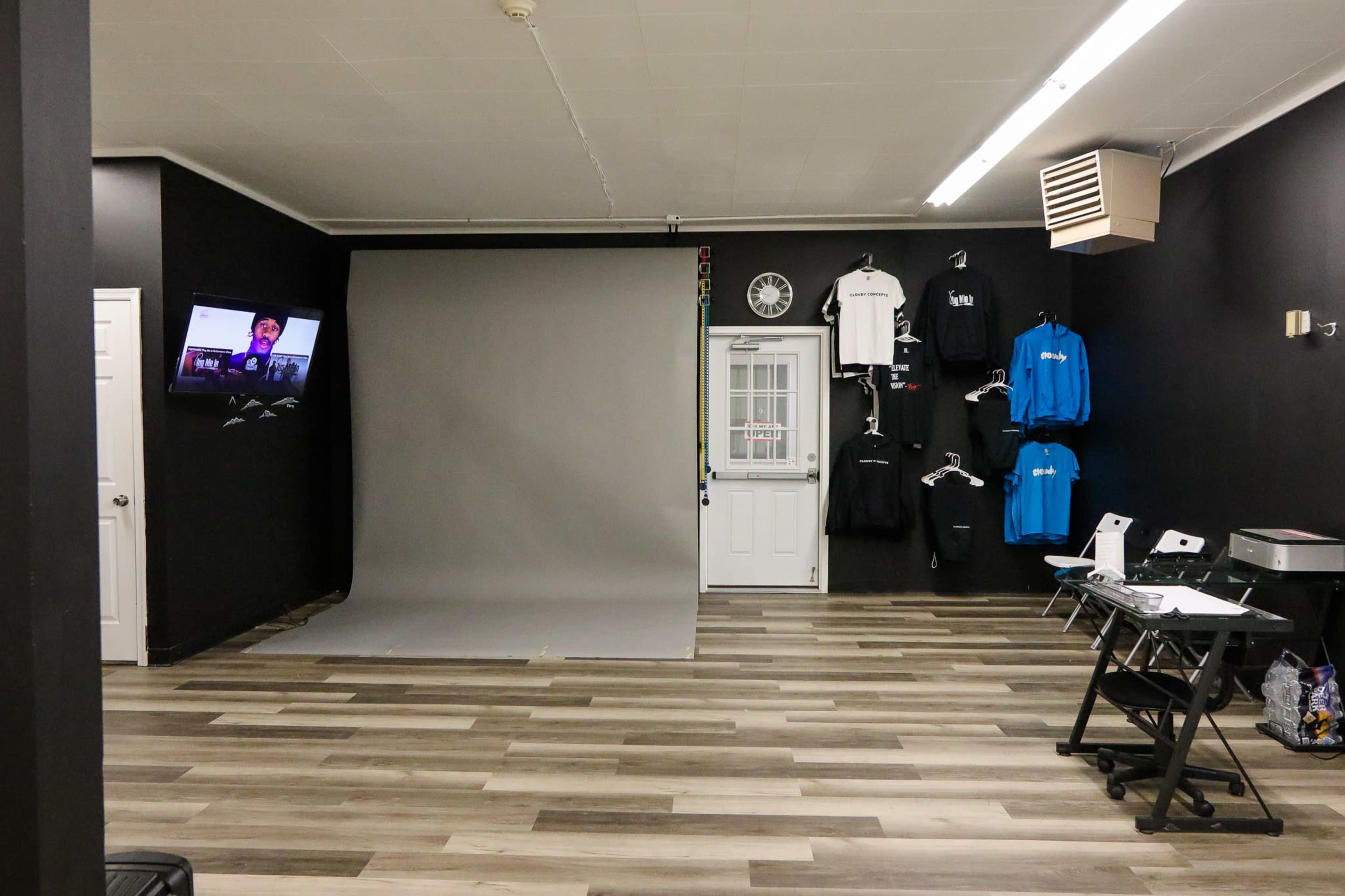 A photography studio featuring a gray backdrop, a television on the wall, and clothing displayed on hangers.