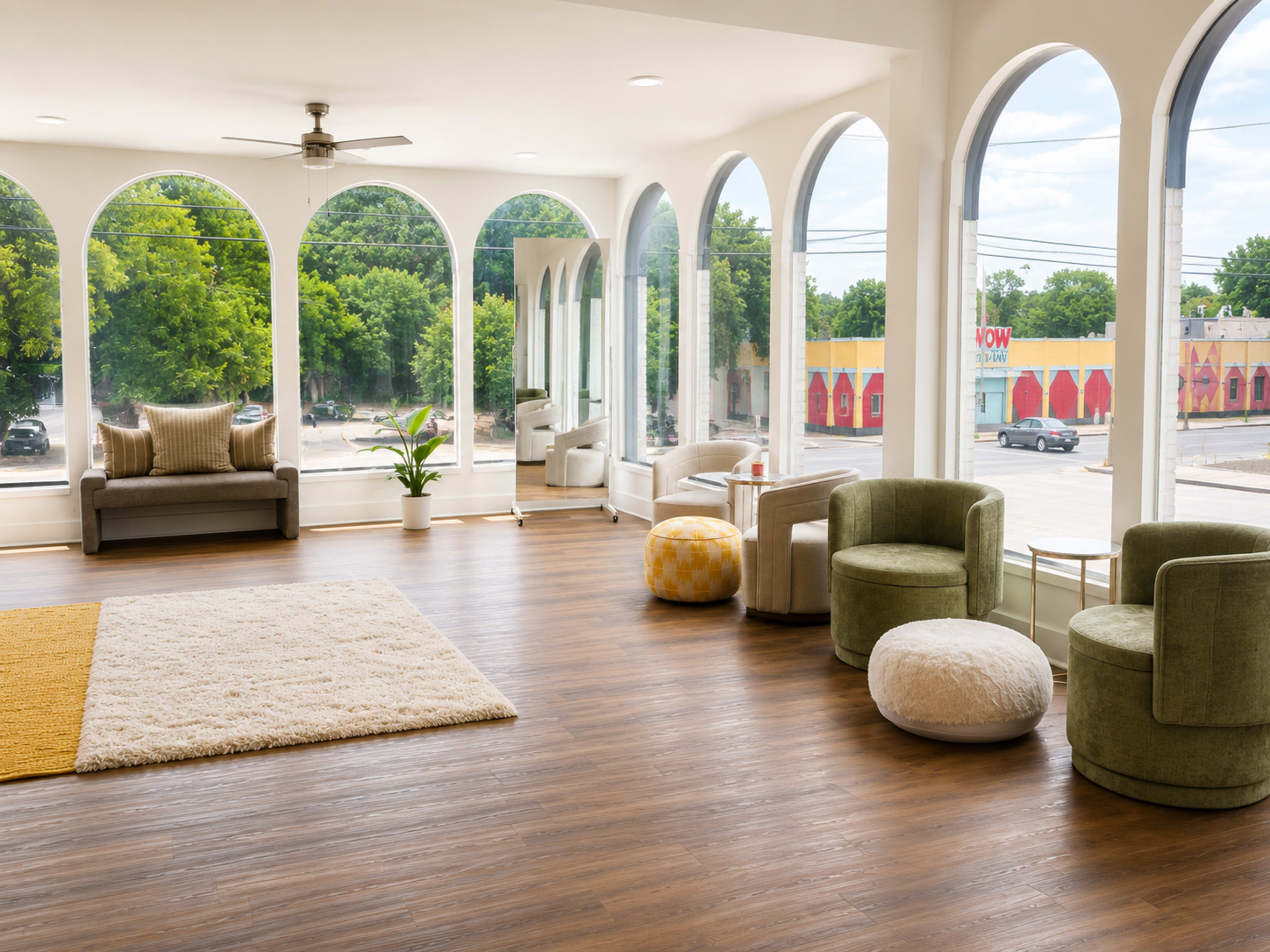 The image shows a spacious interior featuring large arched windows, various seating options including chairs and stools, and a light-colored rug on a wooden floor.