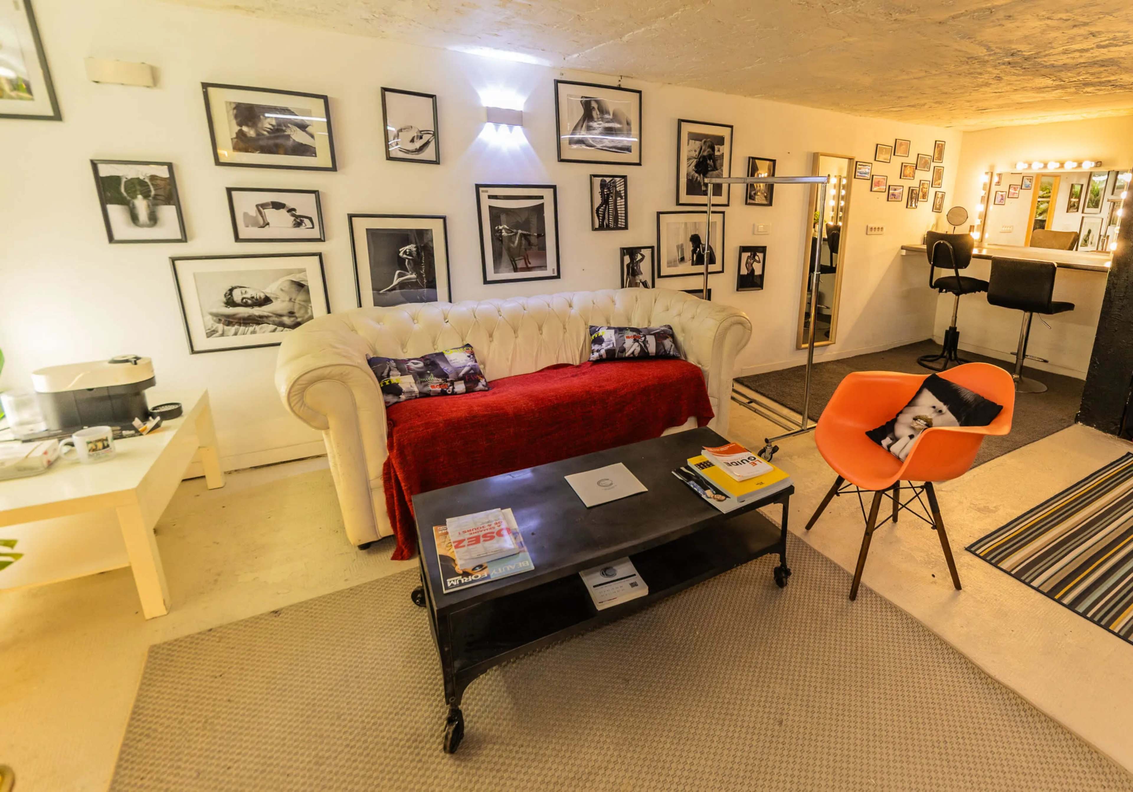 The image shows a modern living room featuring a white tufted sofa, a coffee table with magazines, and various framed photographs on the walls.