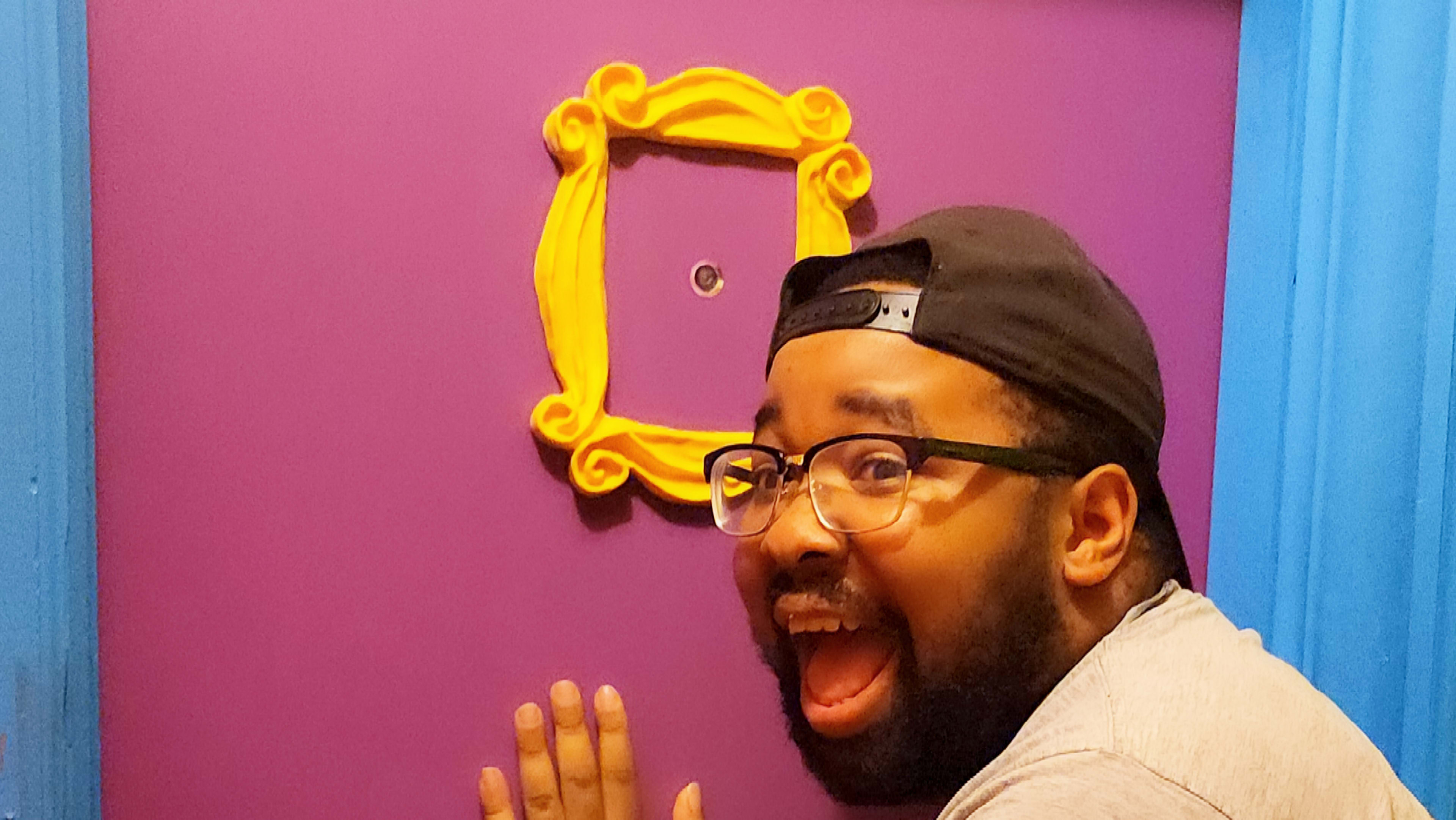 A person stands next to a purple door with a yellow decorative frame around a peephole.