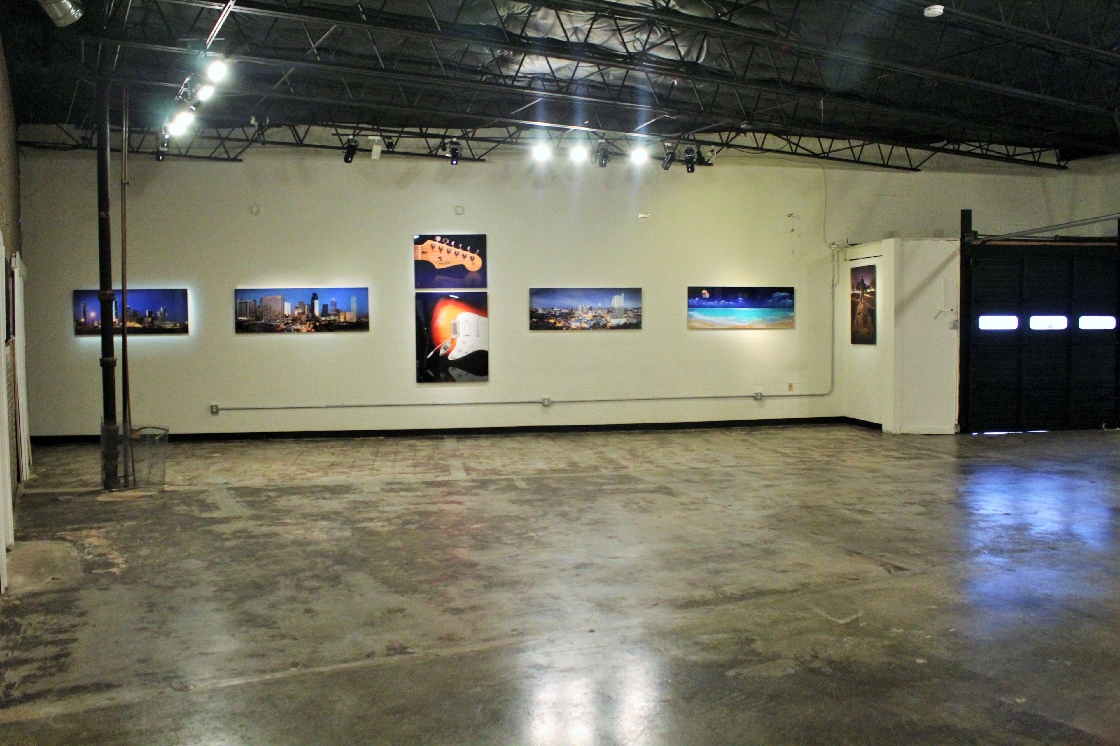 A spacious art gallery with several framed photographs displayed on the white walls and bright lighting above.