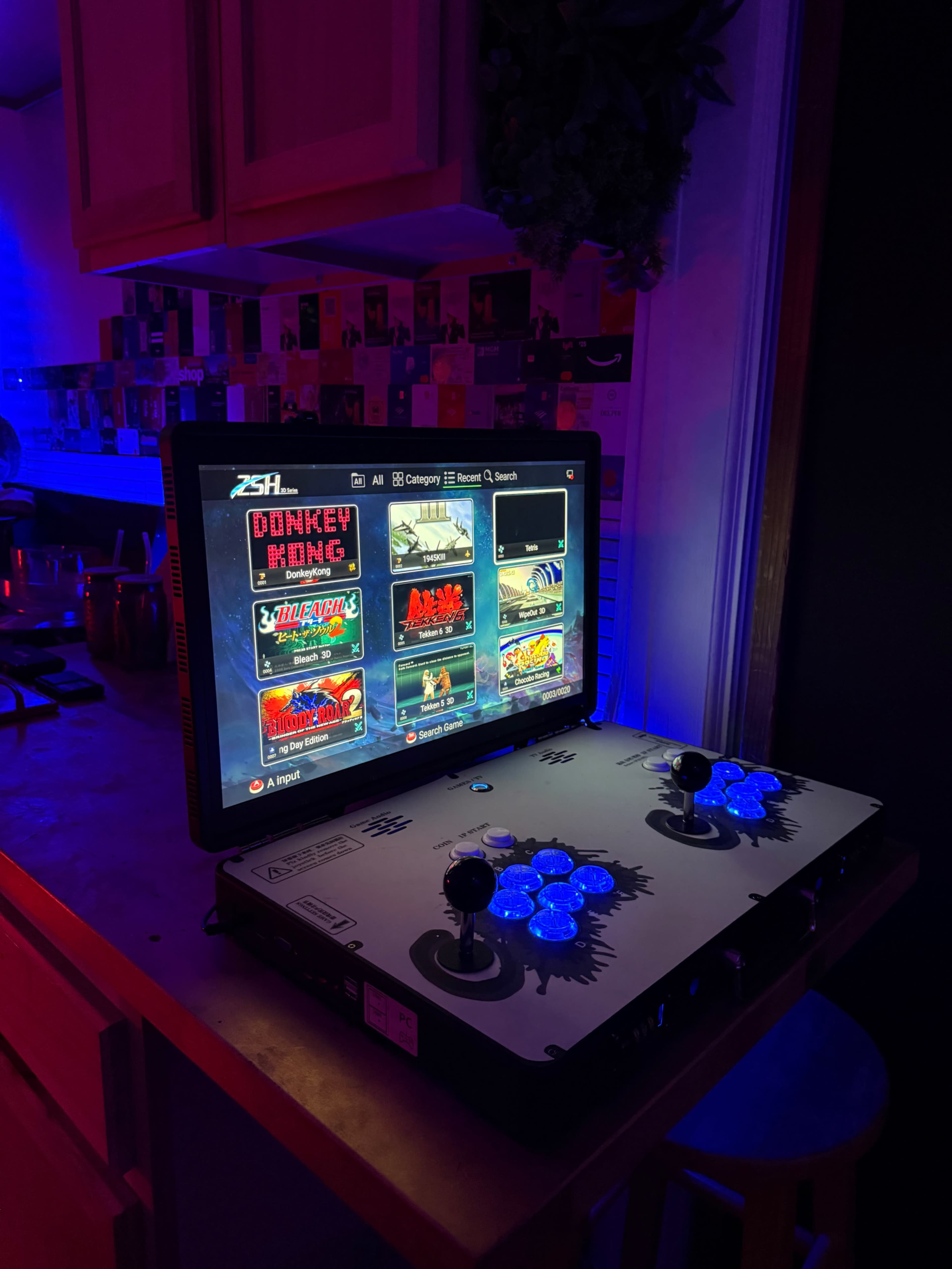 A retro arcade gaming setup displays a screen with various classic game options, illuminated by blue lighting.