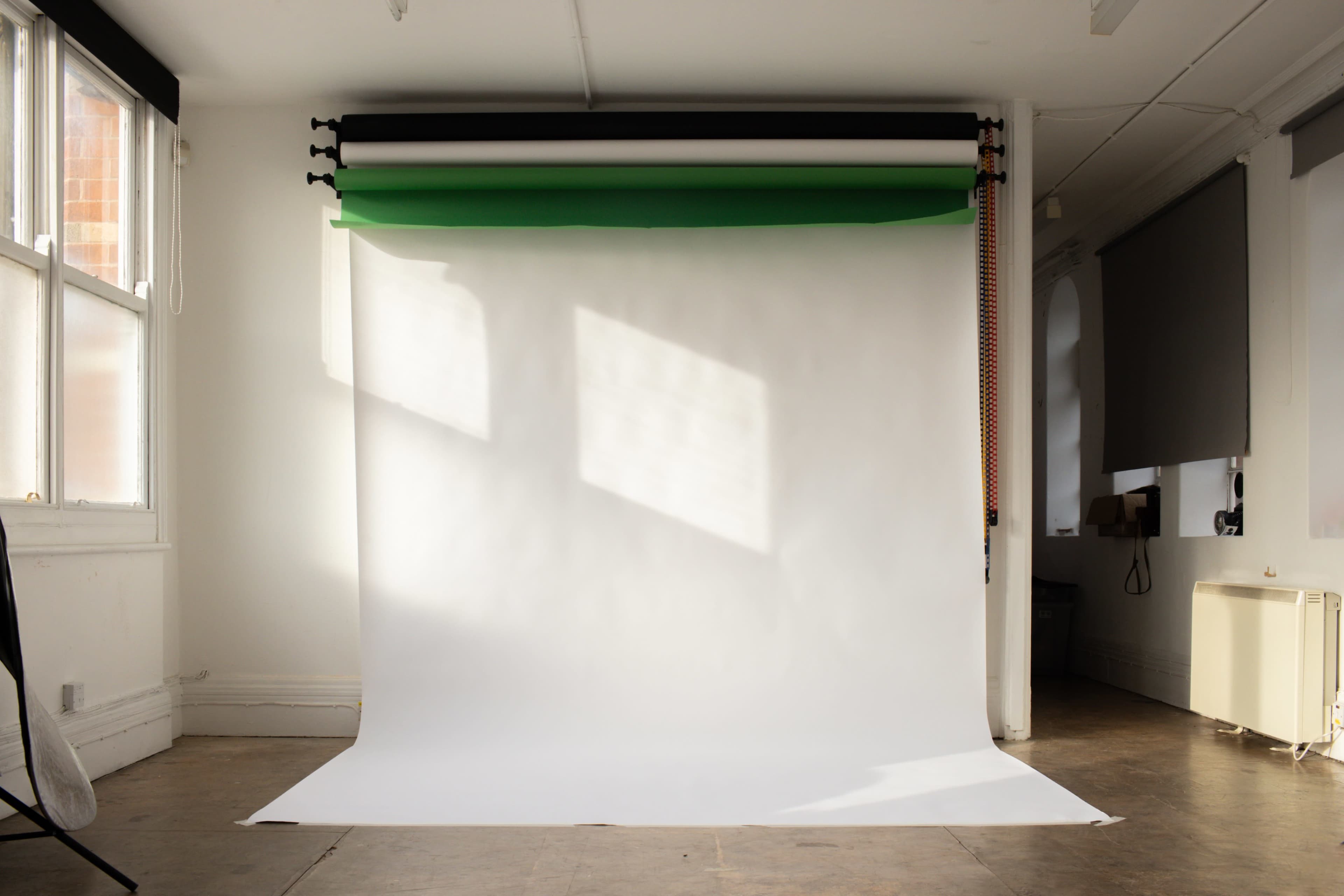 An empty photography studio with a white backdrop and colored paper rolls hanging above.