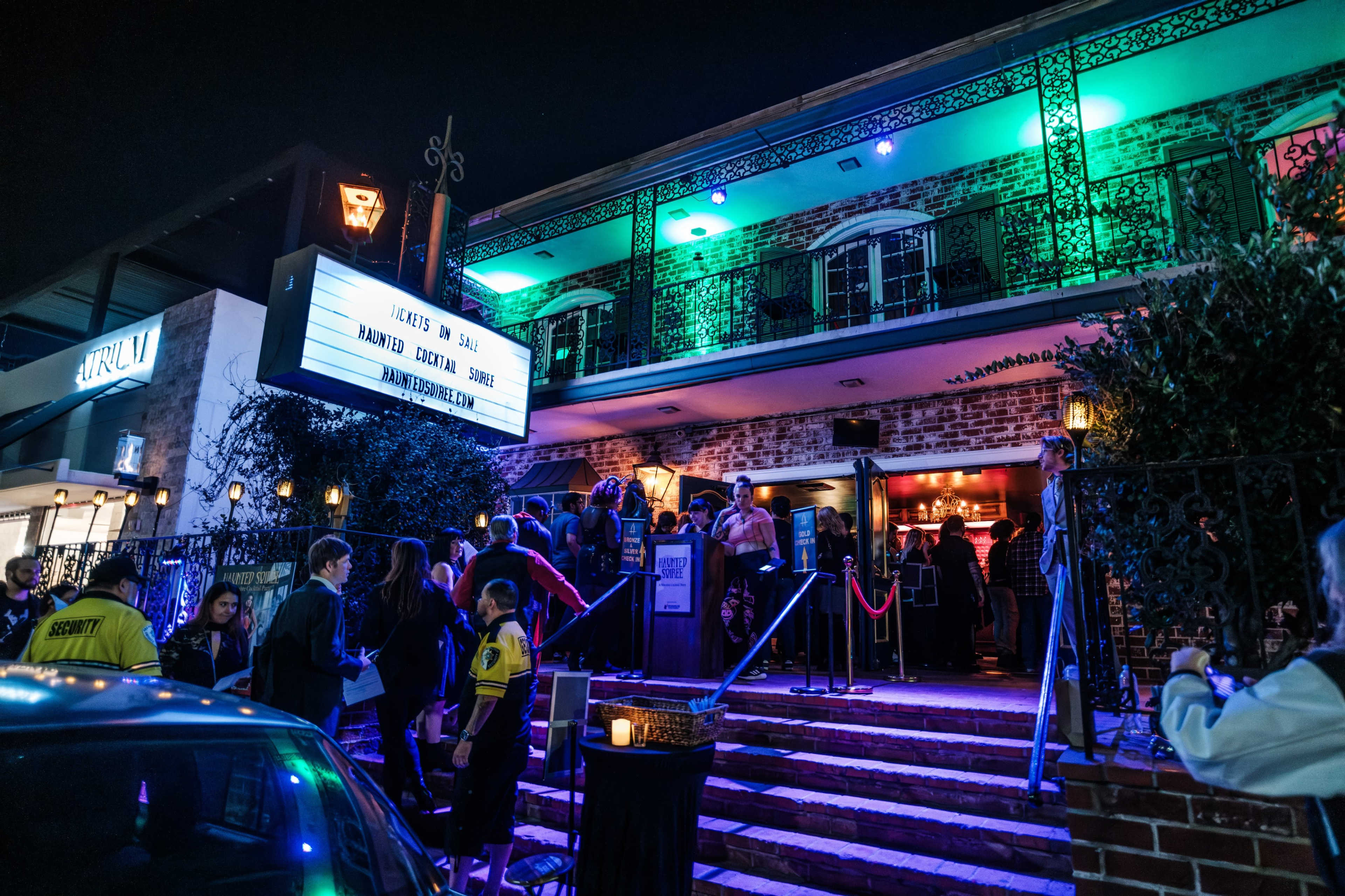 A crowd gathers outside a lively nightclub with vibrant neon lights and a marquee sign at night.