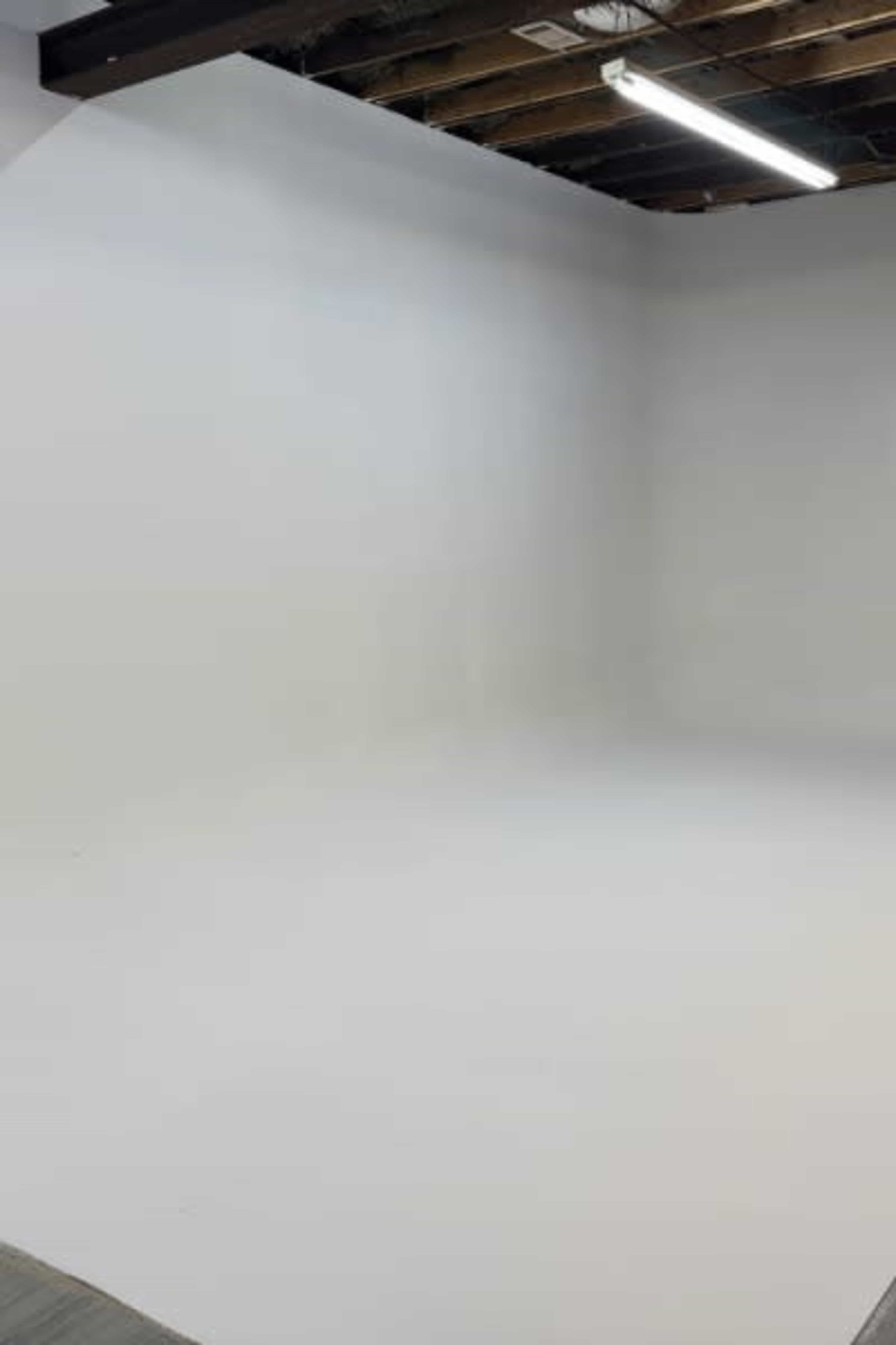 The image shows a largely empty studio space with a white backdrop and exposed ceiling beams.