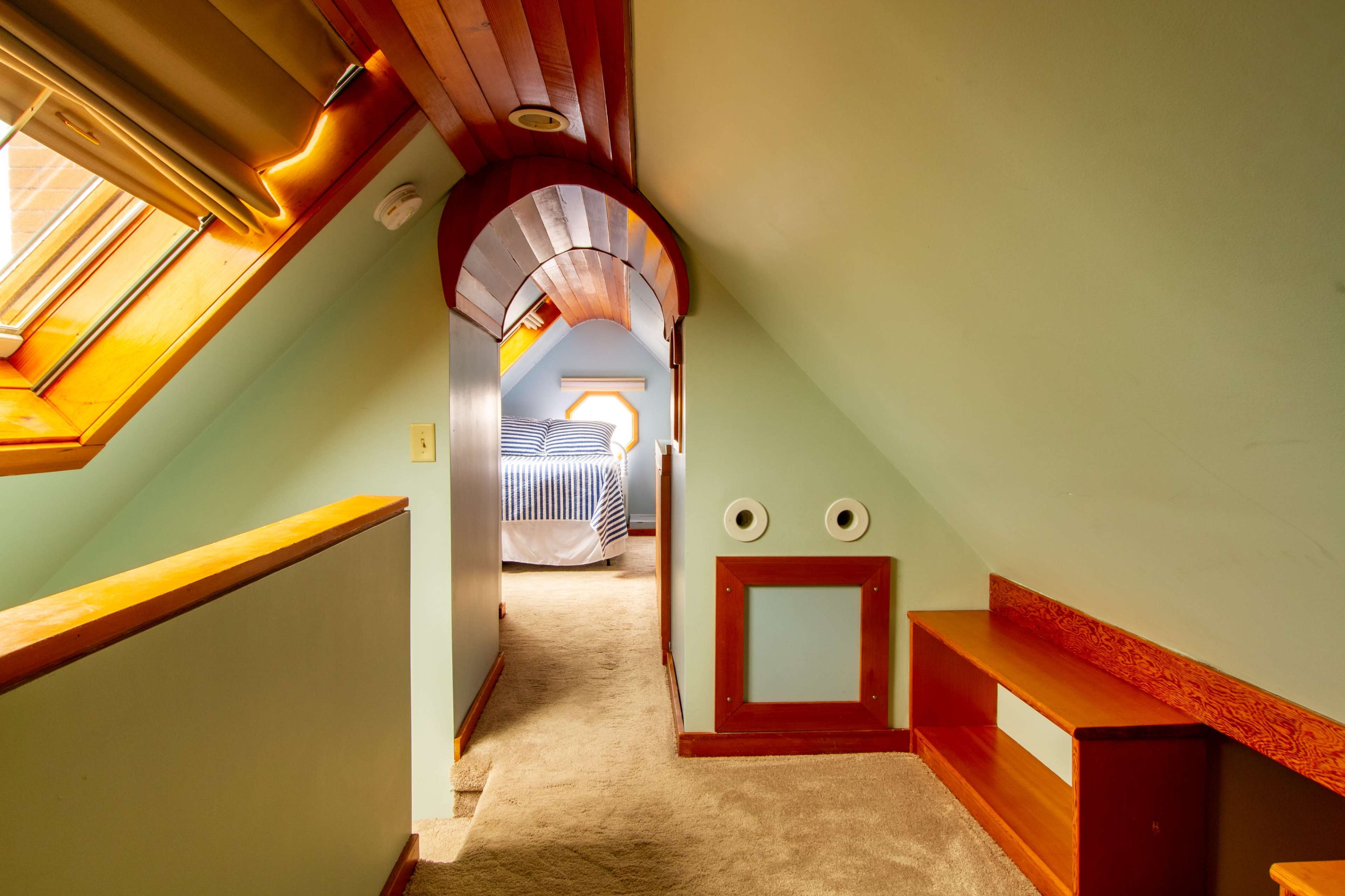 An attic hallway leading to a bedroom with sloped ceilings and a skylight.