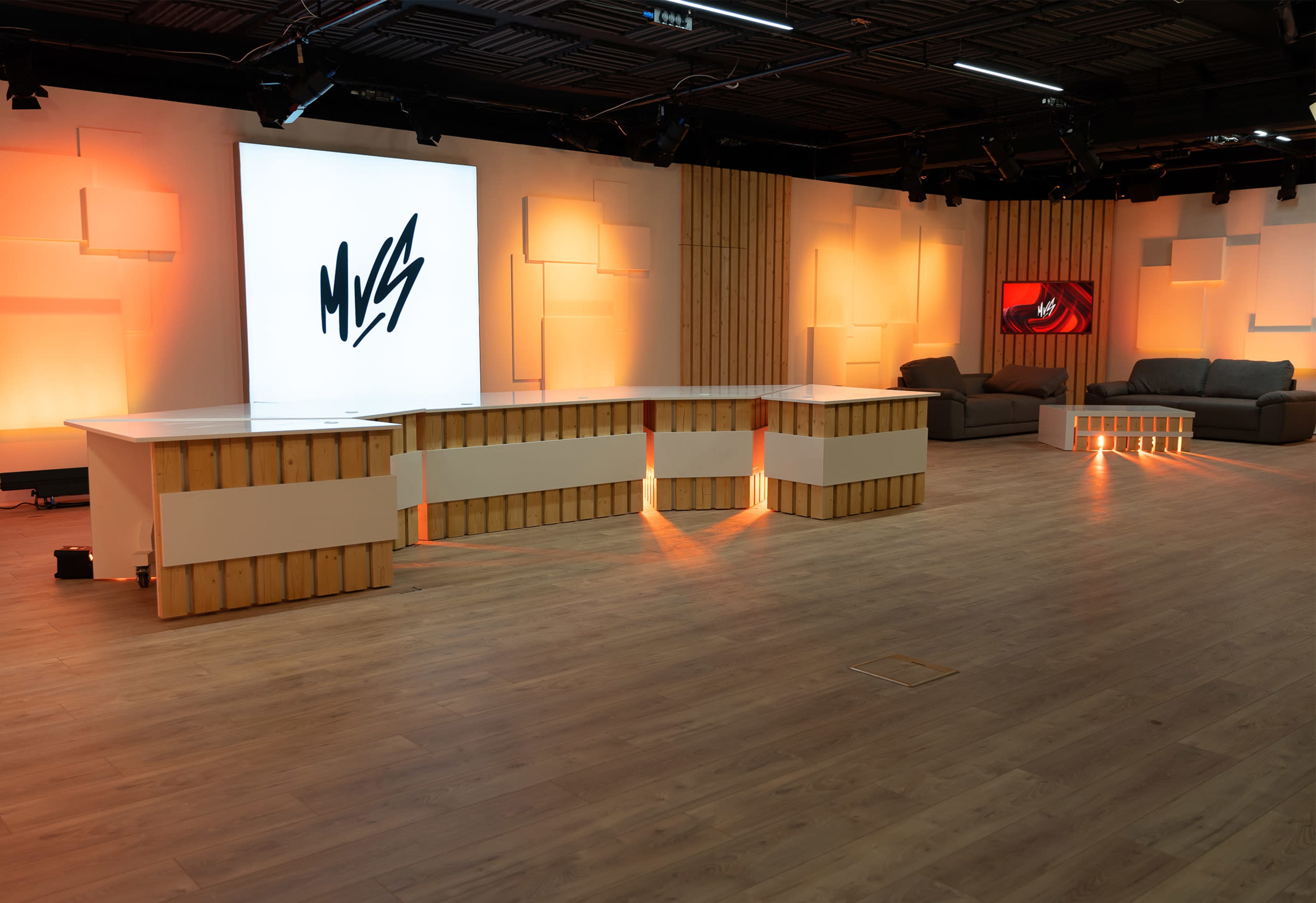 A modern studio space featuring a large logo on a light panel, a sleek reception desk with illuminated accents, and a cozy seating area with a dark sofa.