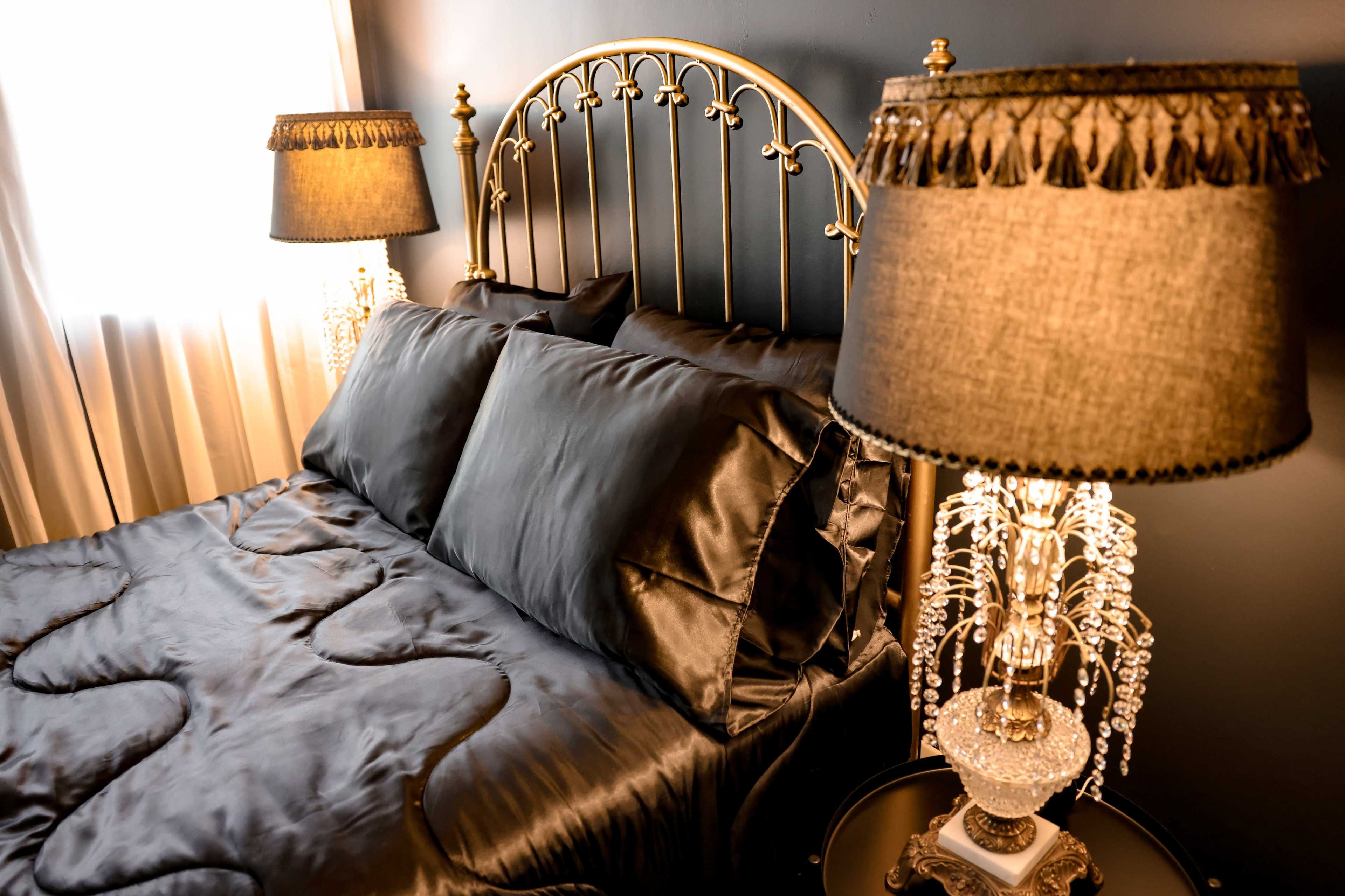 A neatly made bed with black satin bedding and two ornate lamps on nightstands beside it.