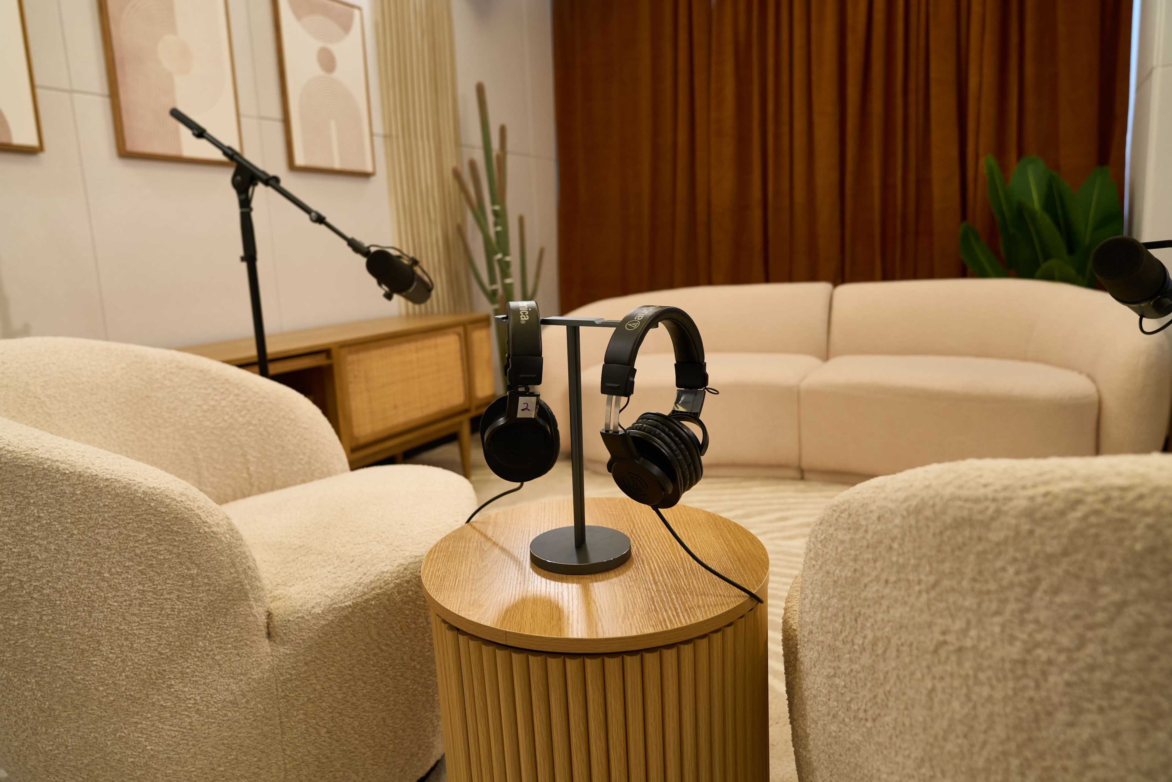 The image shows a cozy recording space featuring a circular couch, two armchairs, and a small round table with a pair of headphones on a stand.