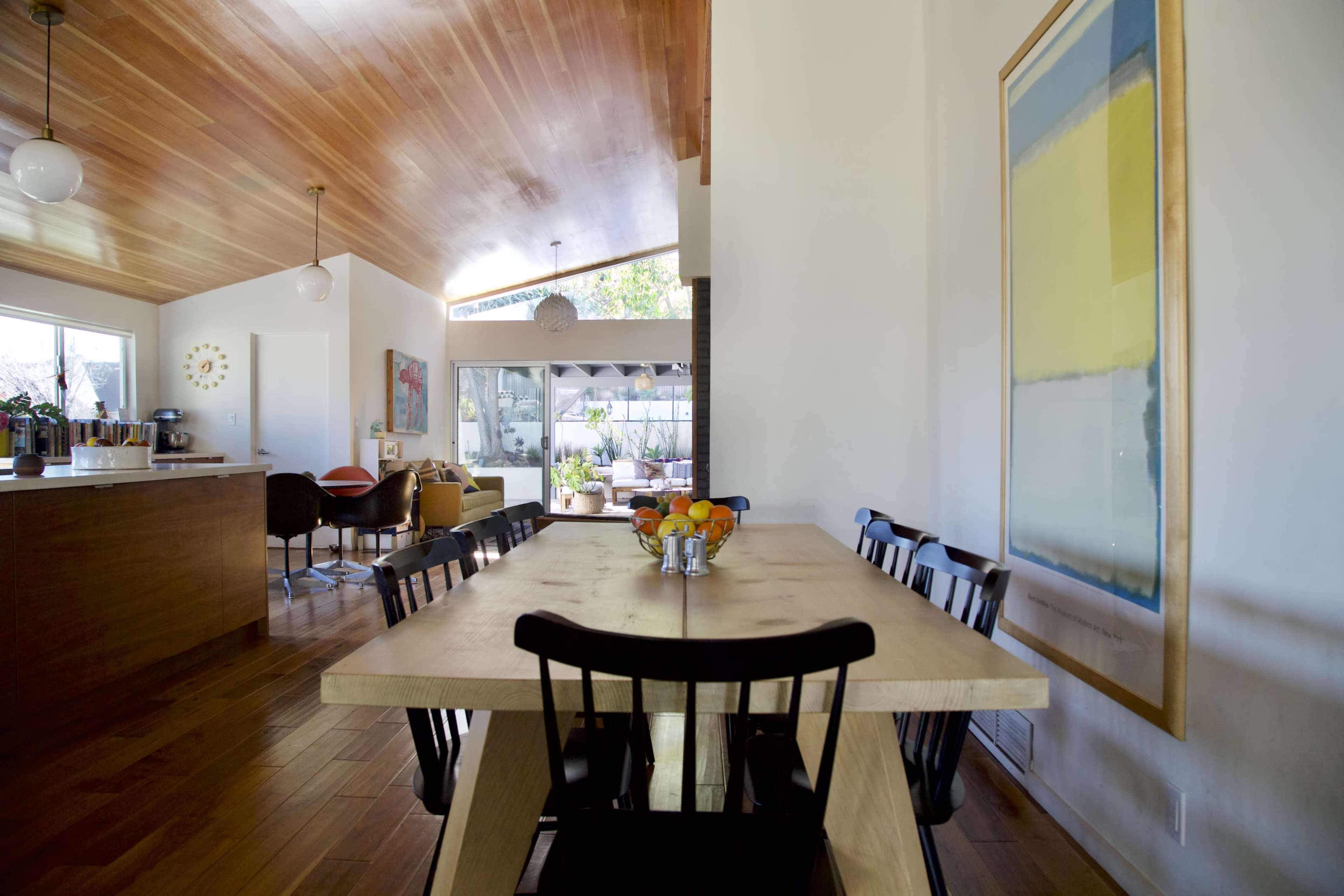 A modern dining area featuring a large wooden table surrounded by black chairs, with a view of a patio through glass sliding doors at the end of the space.