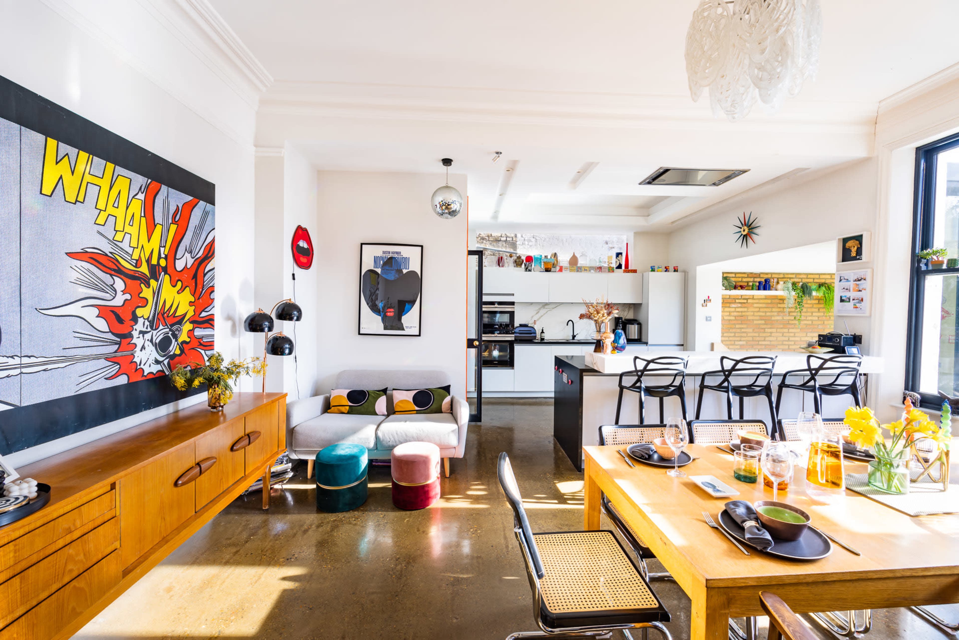 The image shows a modern, open-concept living space with a dining area, kitchen, and colorful furniture accents.