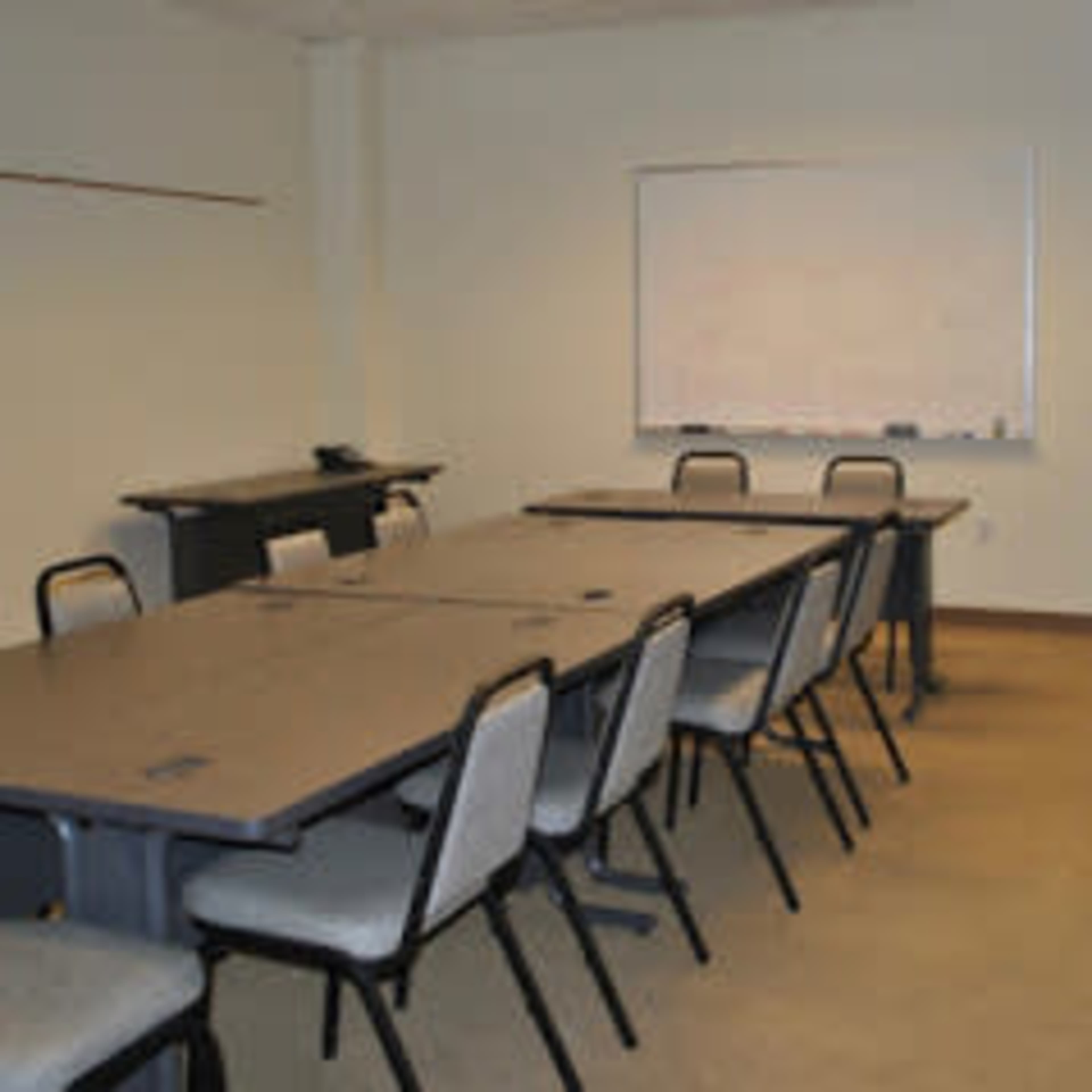 A conference room with a long table surrounded by chairs and a whiteboard on the wall.