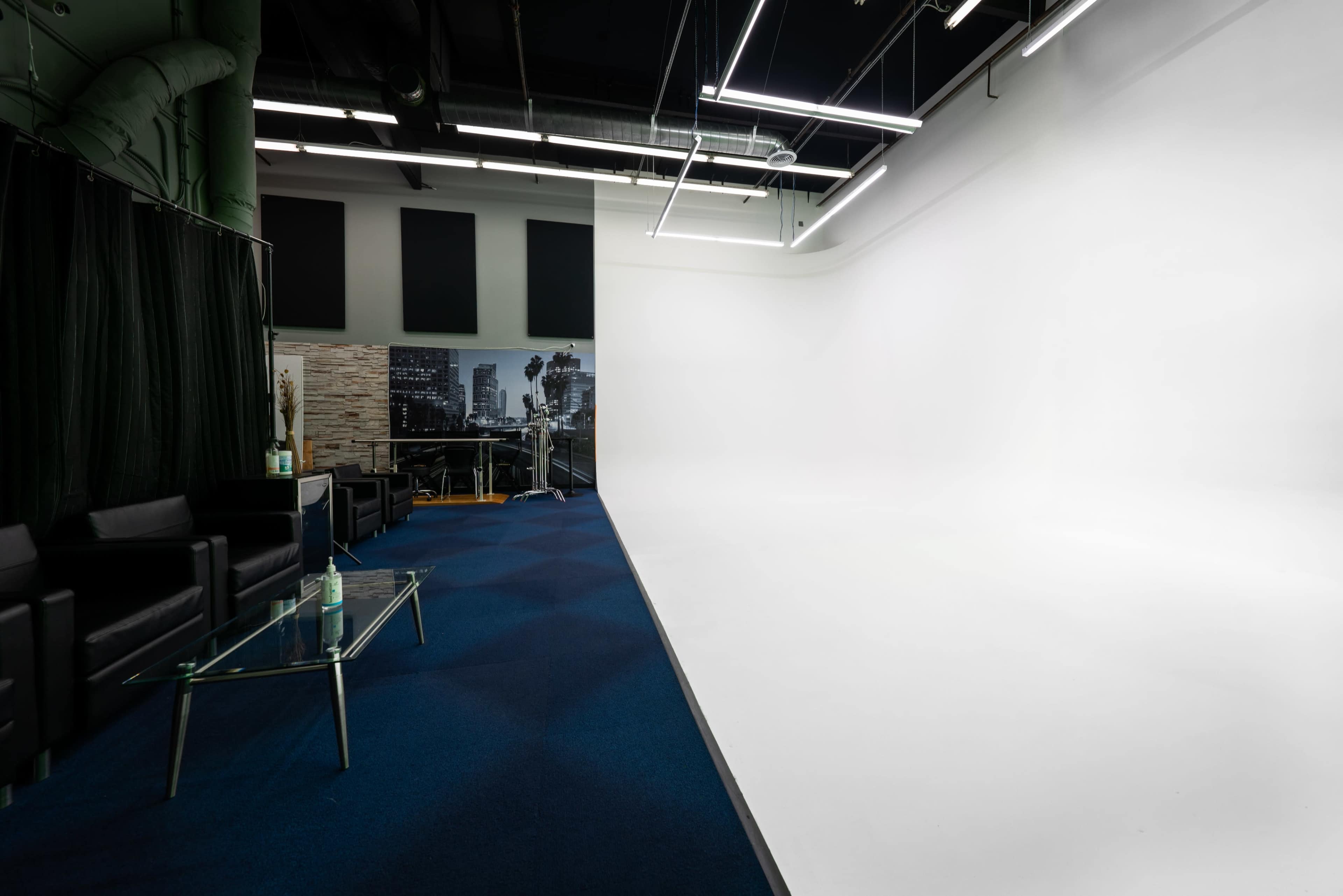 A spacious studio with a white backdrop, black seating area, and blue carpet.