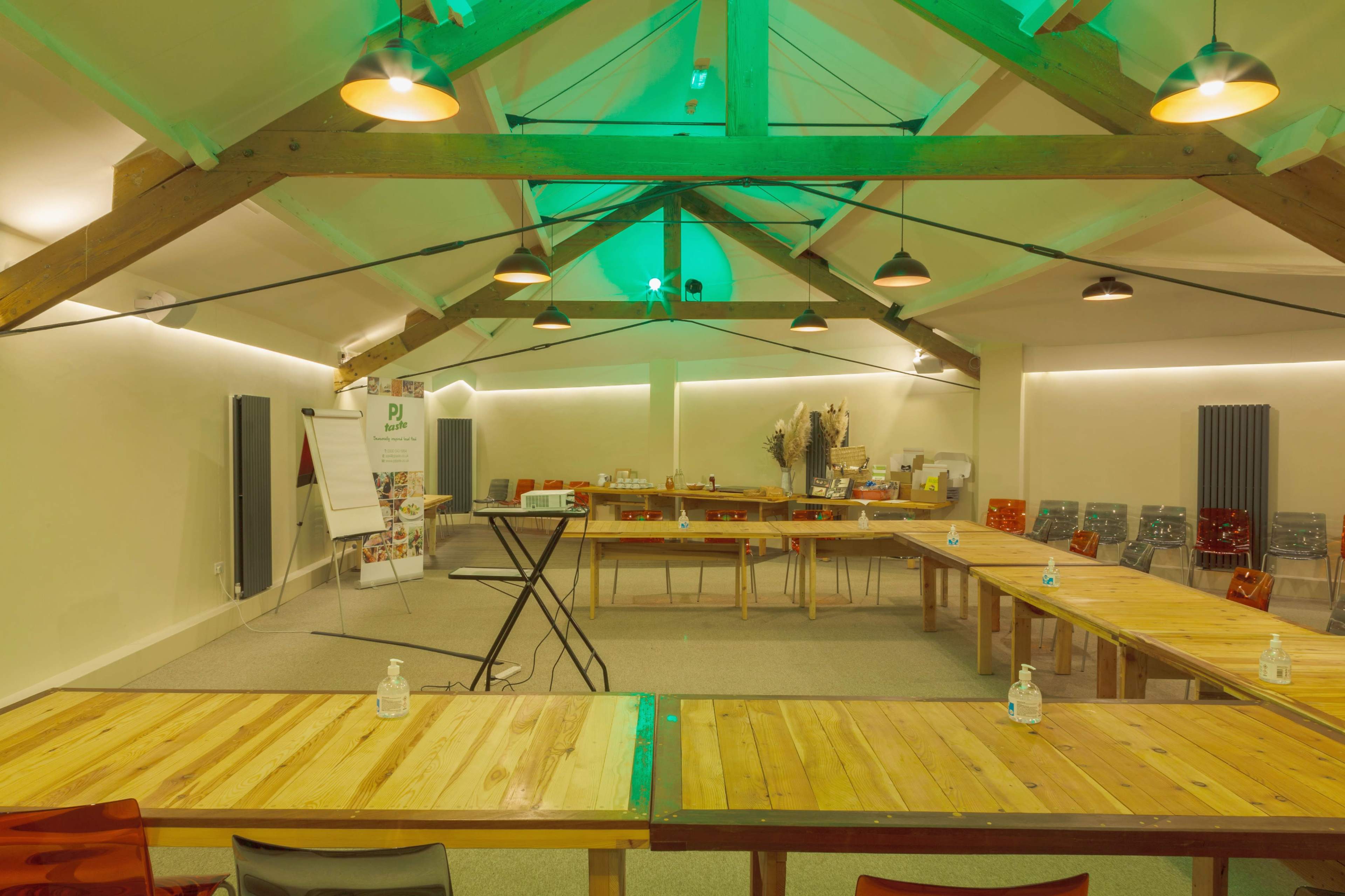 An indoor meeting space with wooden tables arranged in a U-shape, surrounded by colorful chairs, and equipped with audio-visual equipment and hand sanitizer stations.