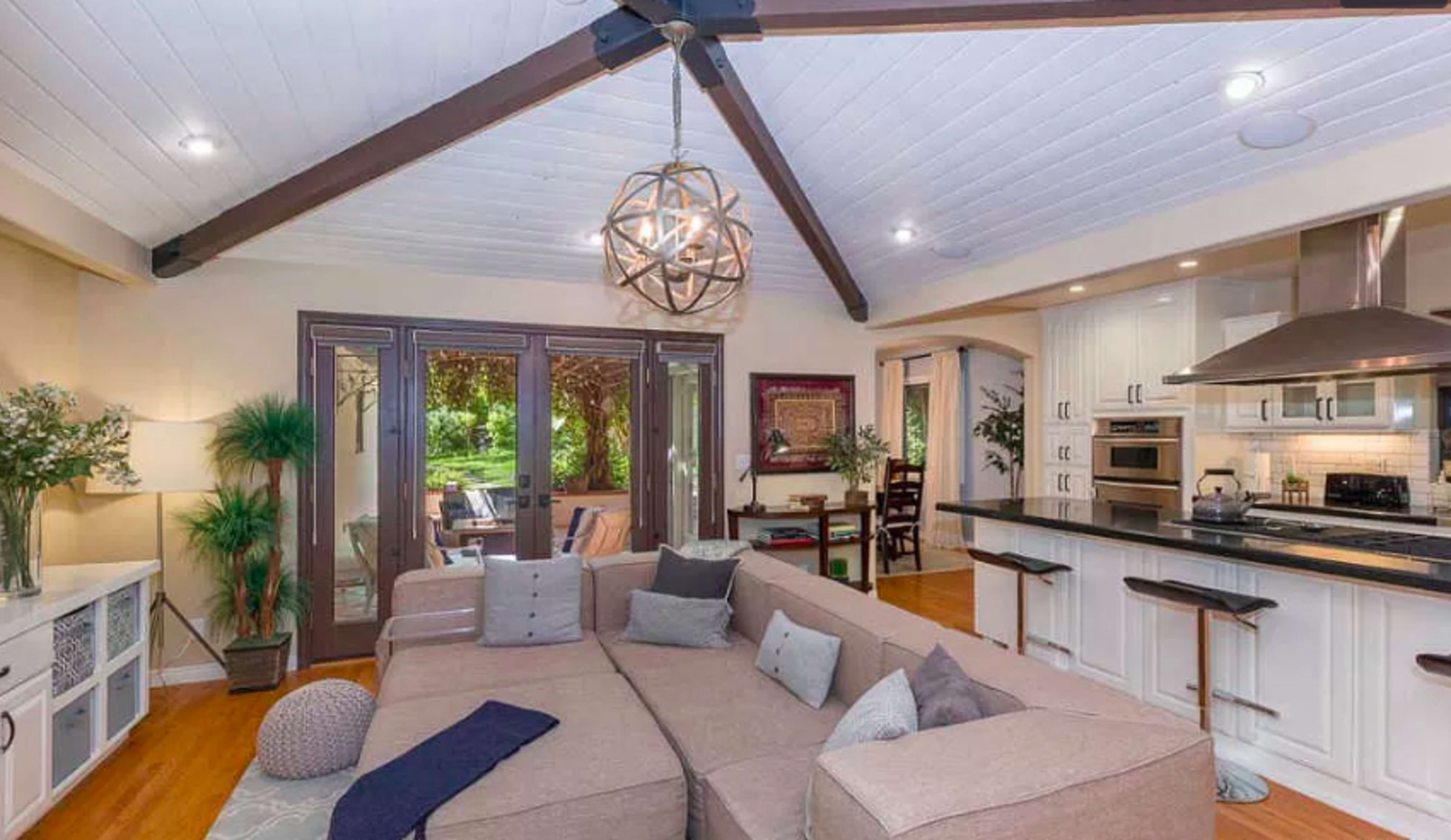 A modern living room features a large sectional sofa, a decorative light fixture, and an open layout that connects to a kitchen area.