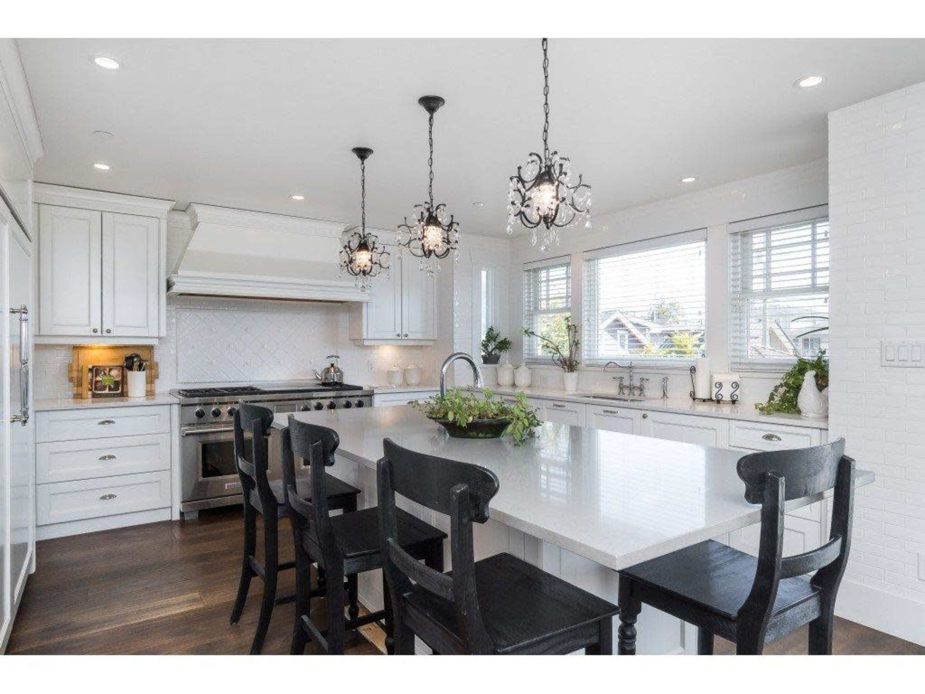 A modern kitchen features a large island with black chairs, white cabinetry, and pendant lighting.