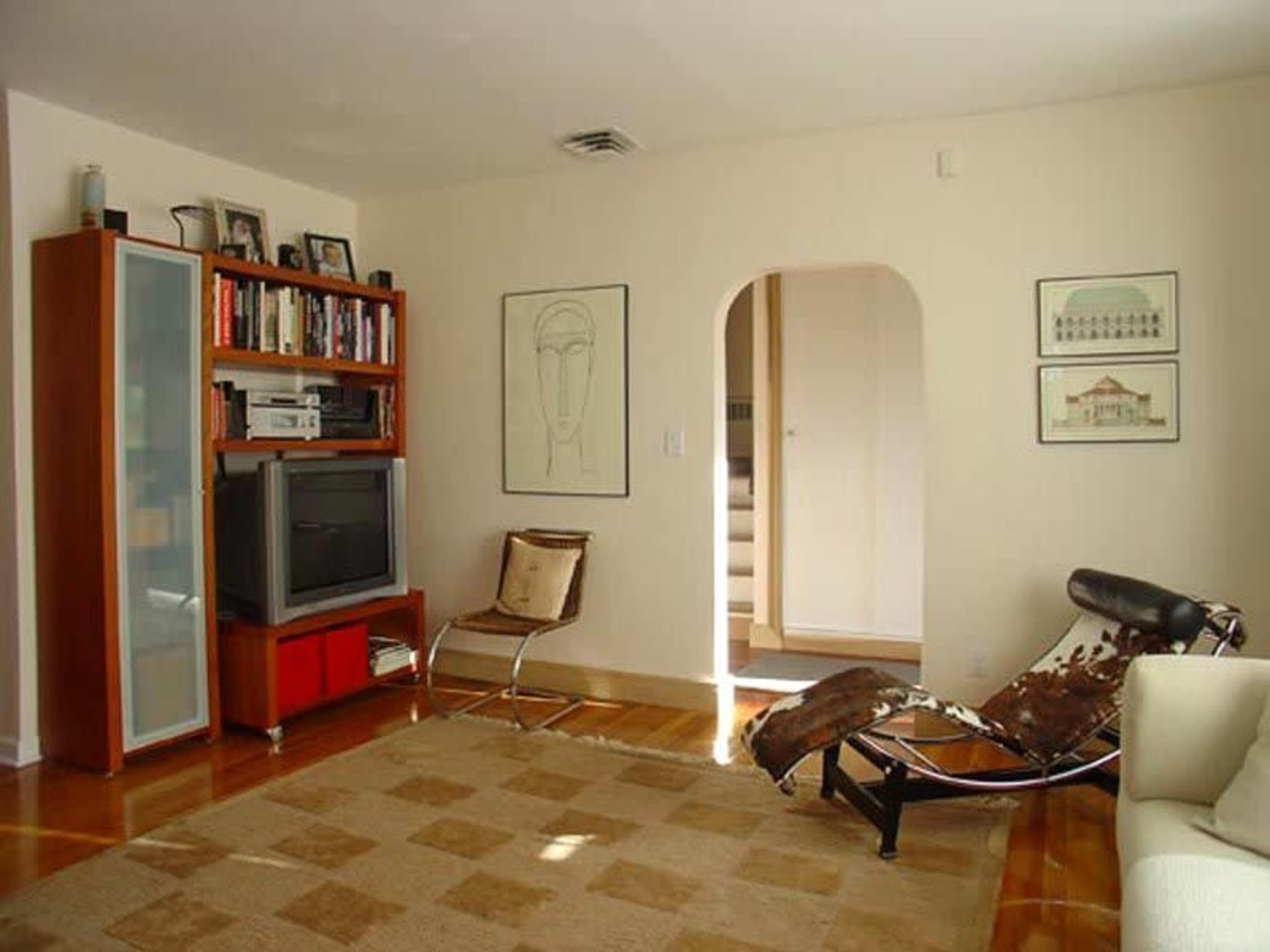 A modern living room with a television, bookshelves, and a comfortable seating area, featuring a patterned rug on a wooden floor.