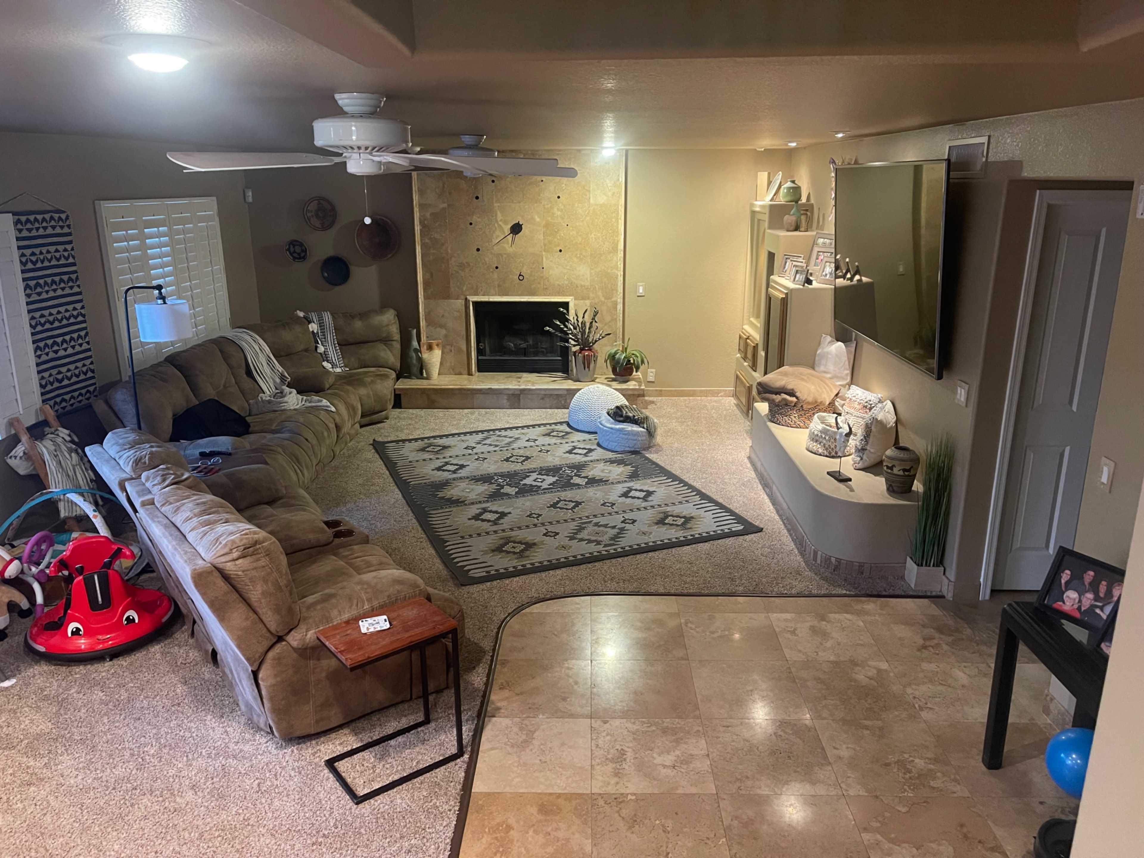 A living room with a large sectional couch, a coffee table, a fireplace, and a TV mounted on the wall, along with a patterned area rug.