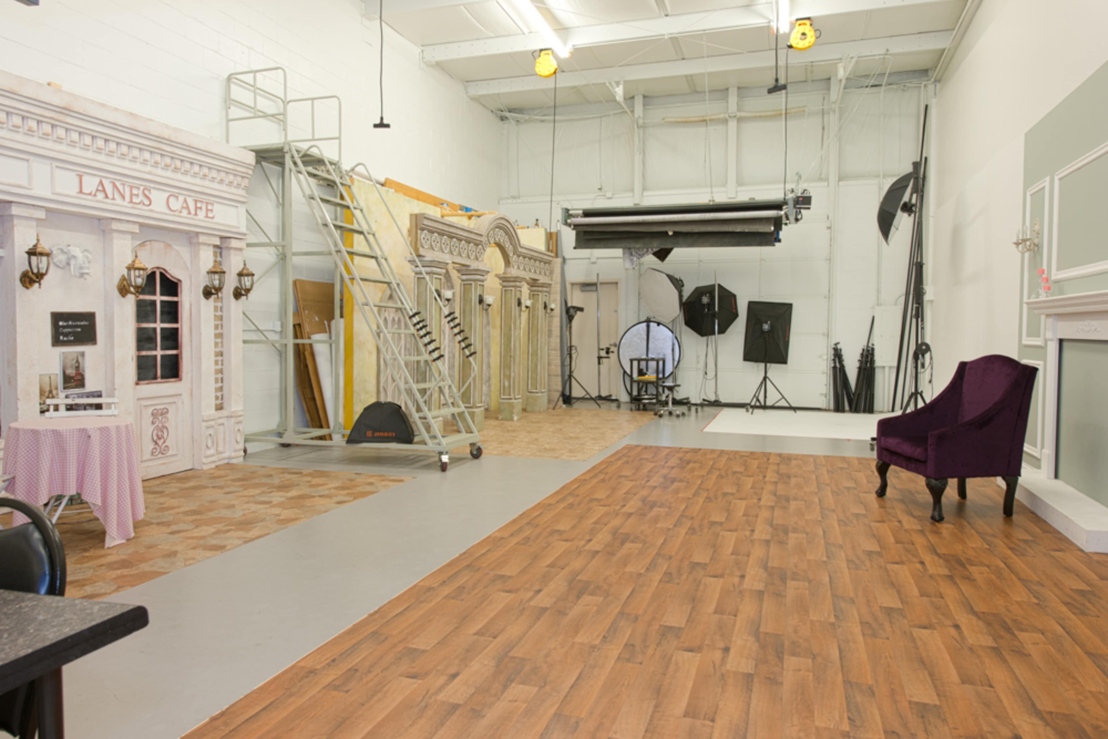 A spacious photography studio with a café setup, a ladder, and various backdrops, including a plain white area for shooting.