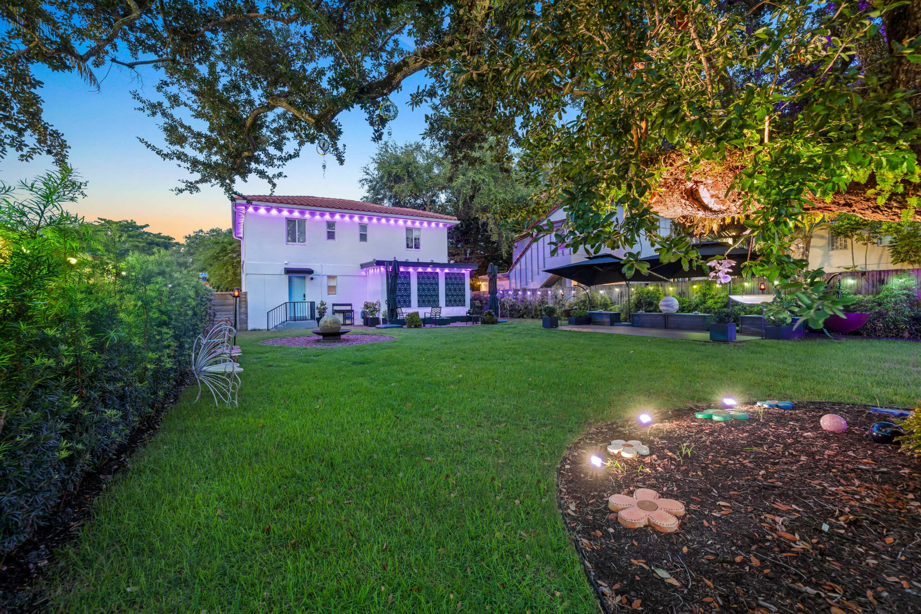 The image shows a two-story white house with outdoor lighting, surrounded by a green lawn and landscaped areas.