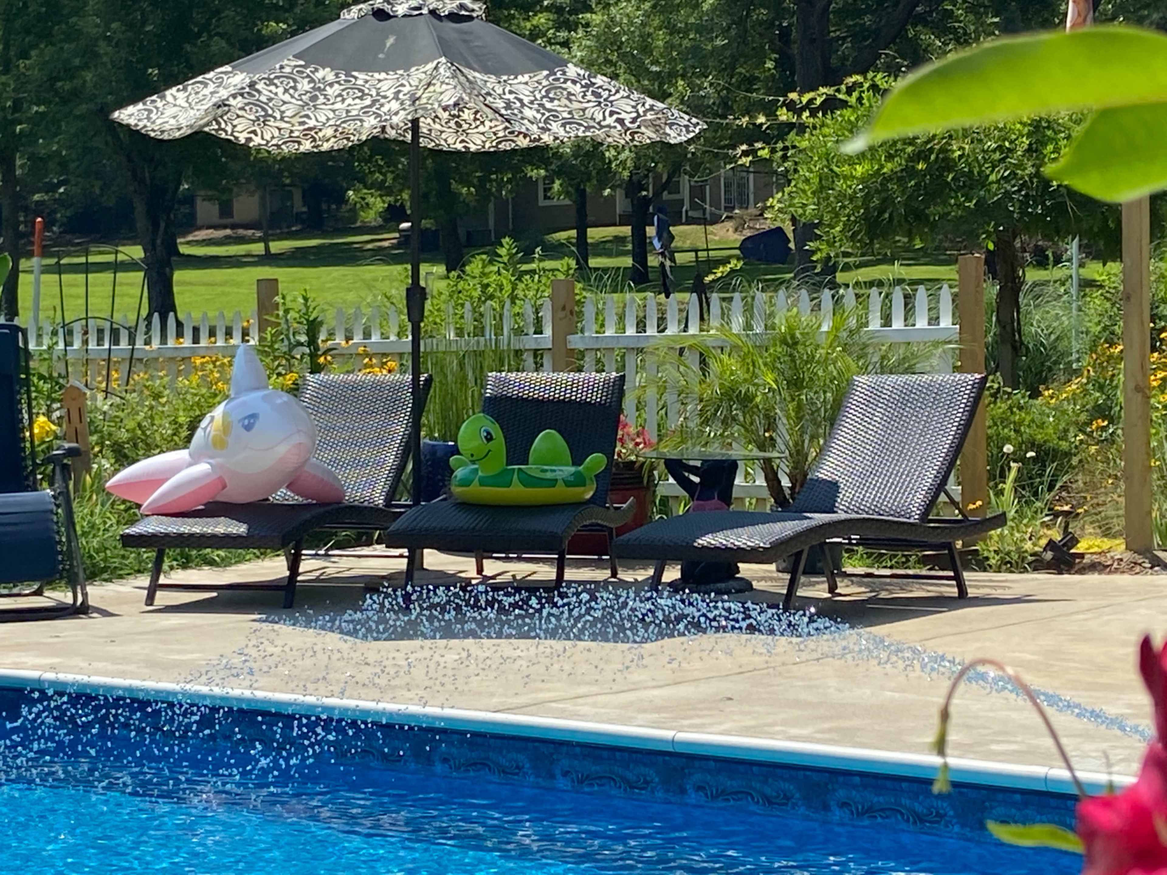 Two lounge chairs sit by a swimming pool, adorned with inflatable pool toys, under an umbrella.