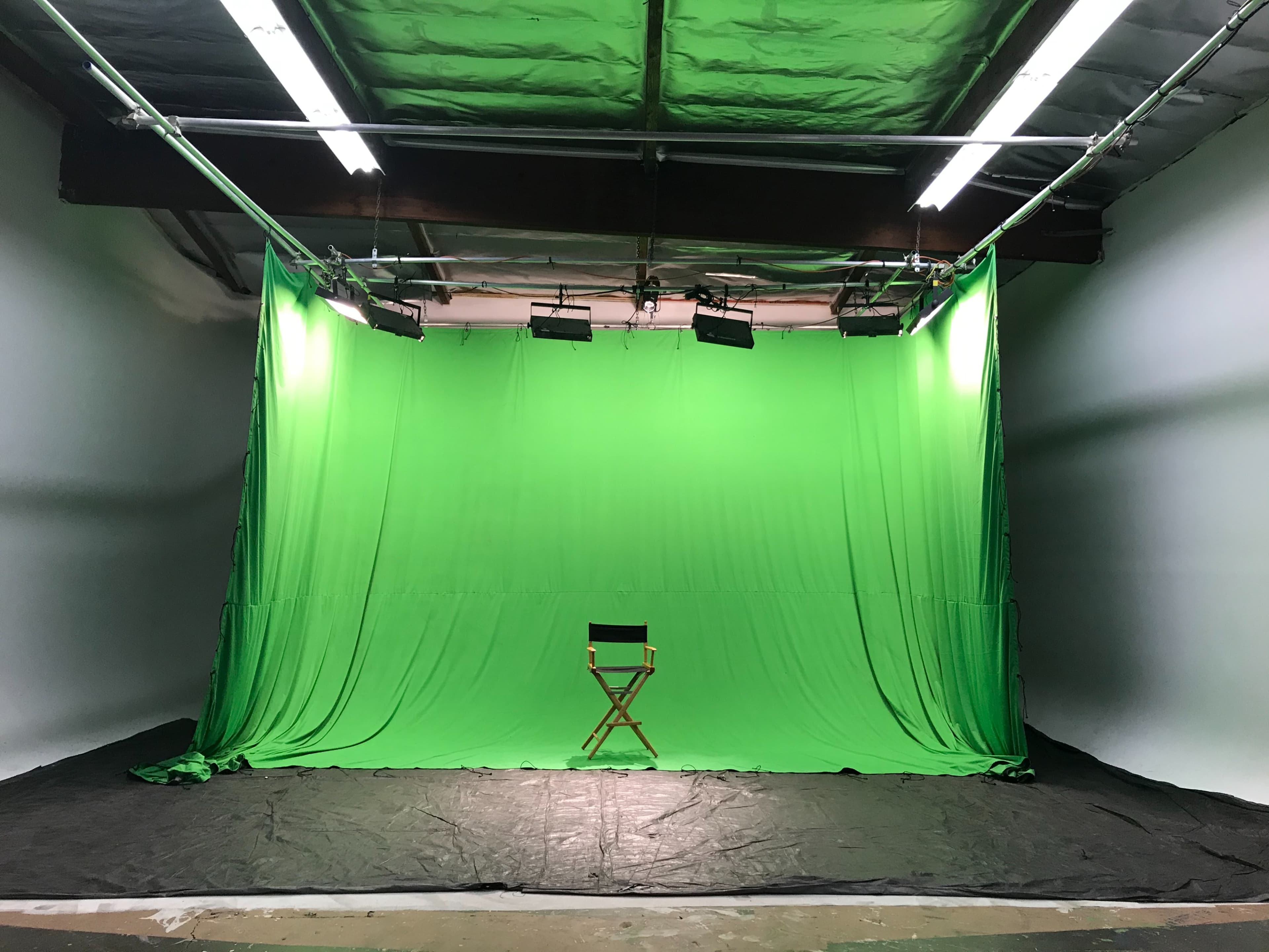 A studio with a green screen backdrop and a director's chair in the center.