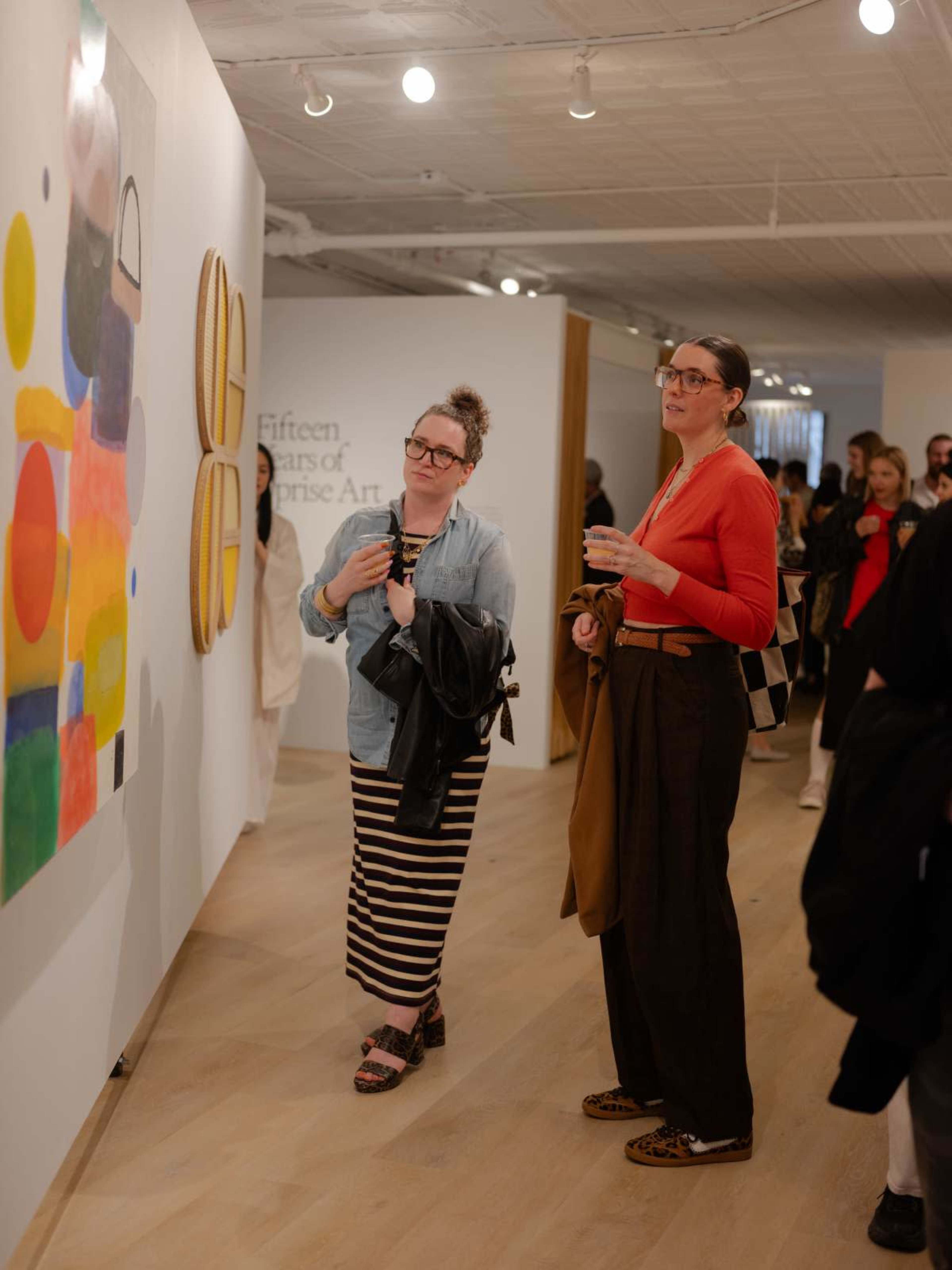 Two women observe abstract artwork on a gallery wall during an art exhibition.