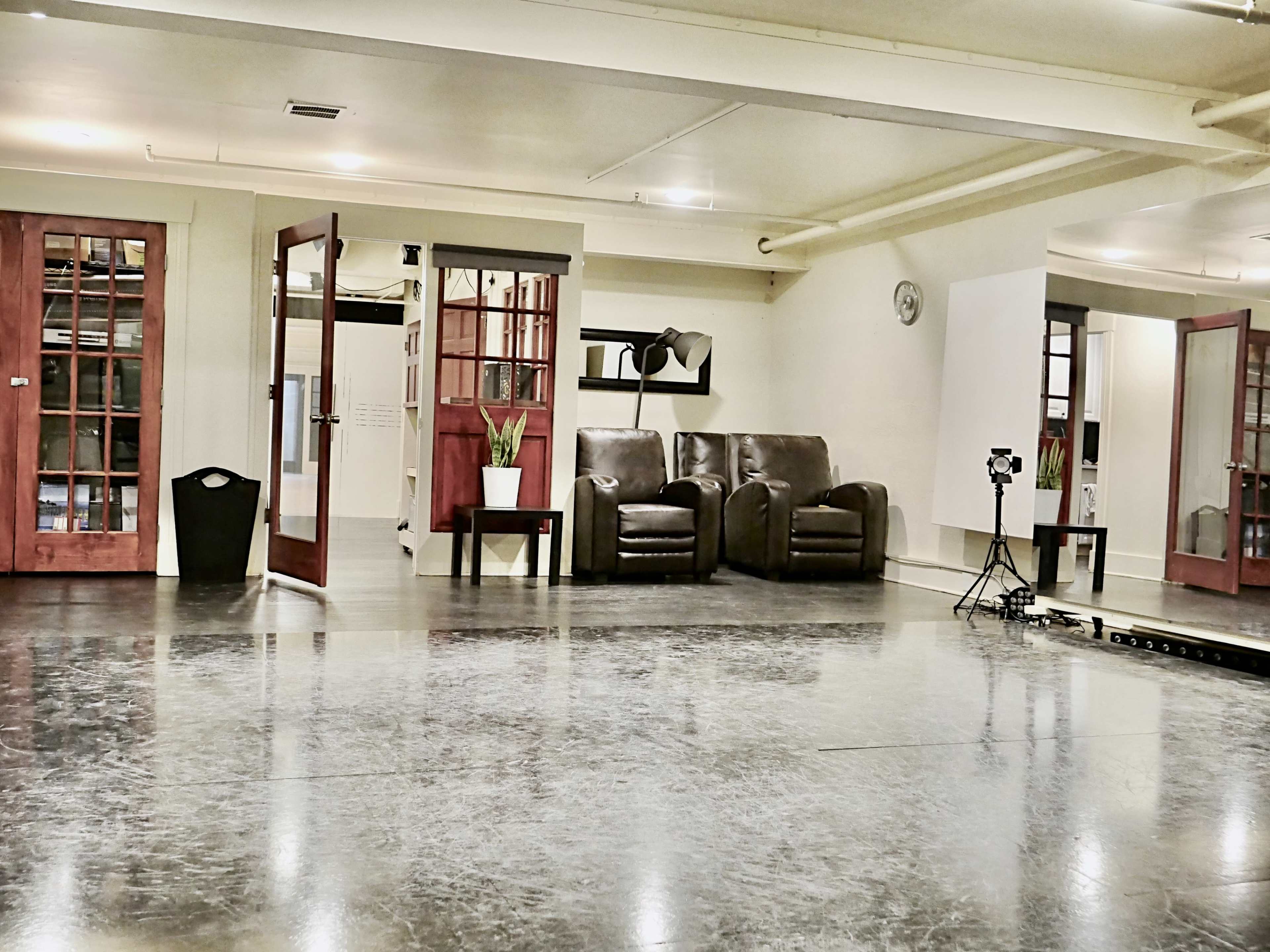 The image shows a spacious dance studio with a polished floor, two leather chairs, and mirrored walls, illuminated by overhead lighting.