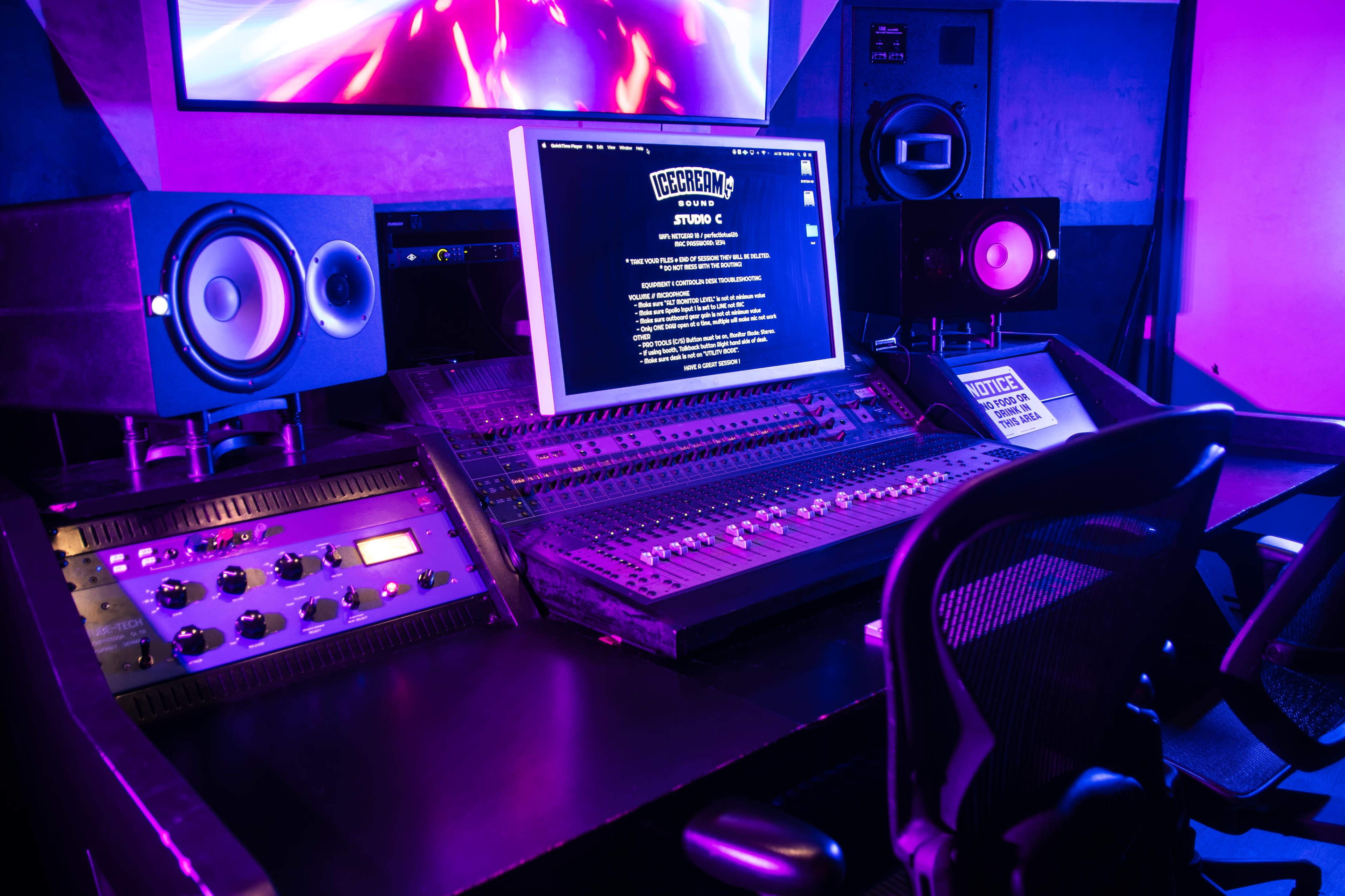 A digital audio workstation filled with sound mixing equipment and speakers is displayed under purple lighting in a music studio.