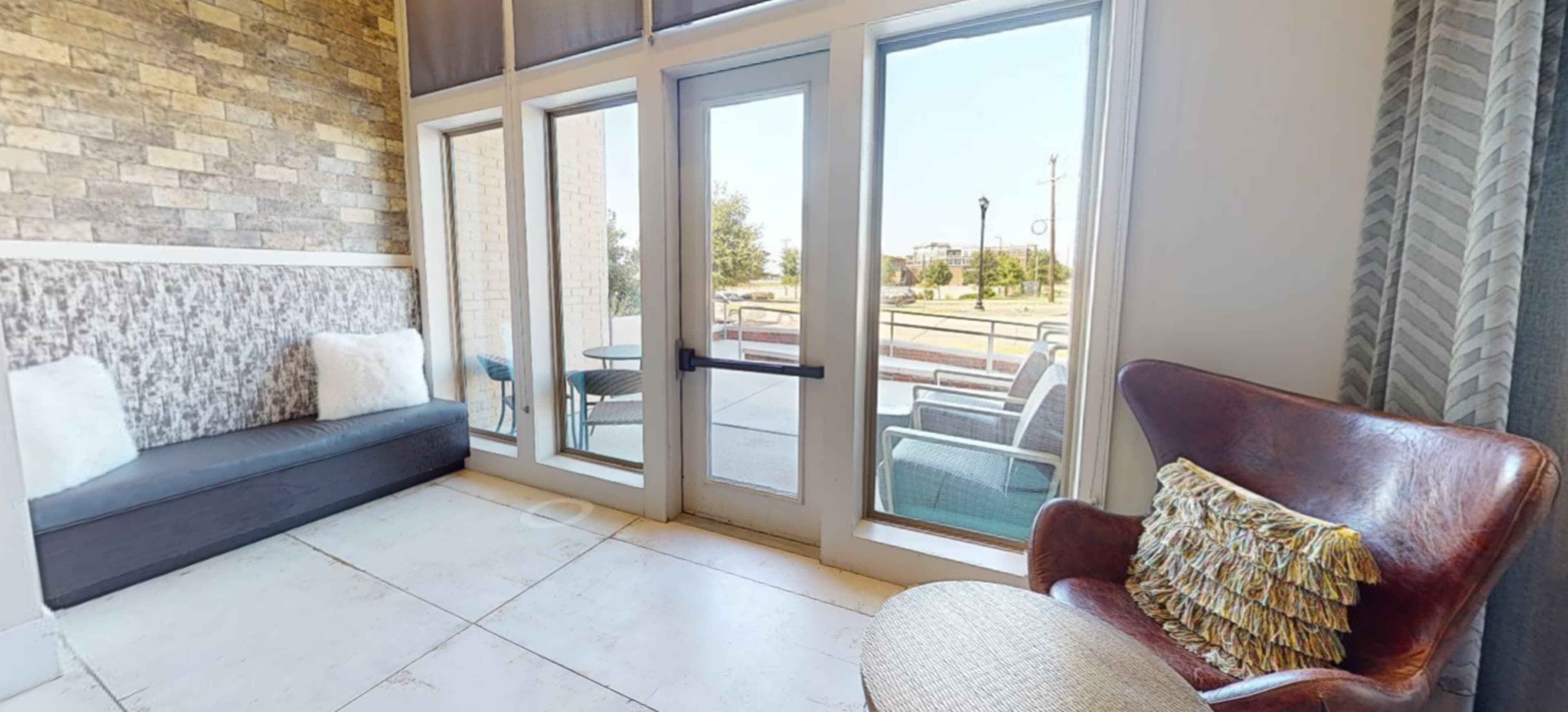 A cozy seating area with large windows, a wooden bench, and an armchair with decorative pillows, overlooking an outdoor space.