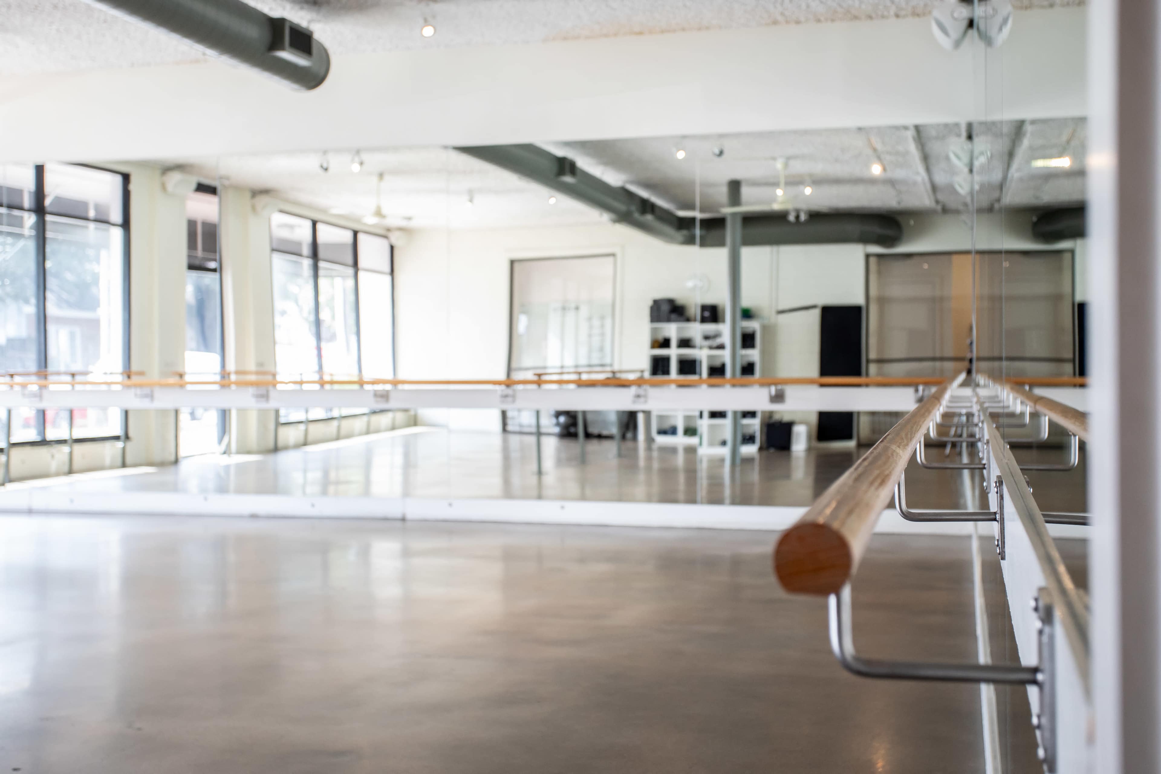 The image shows an empty dance studio with mirrored walls and a wooden ballet barre.
