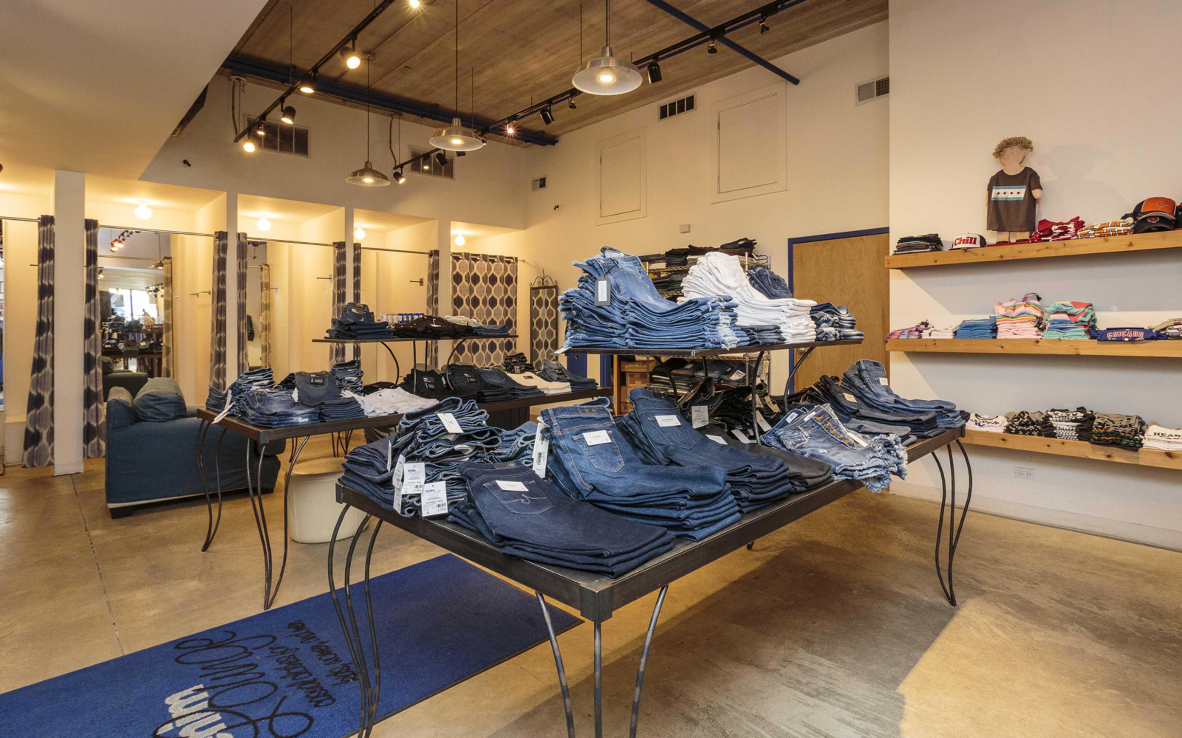 The image shows a retail clothing store interior with neatly stacked denim jeans on tables and shelves displaying various apparel items.