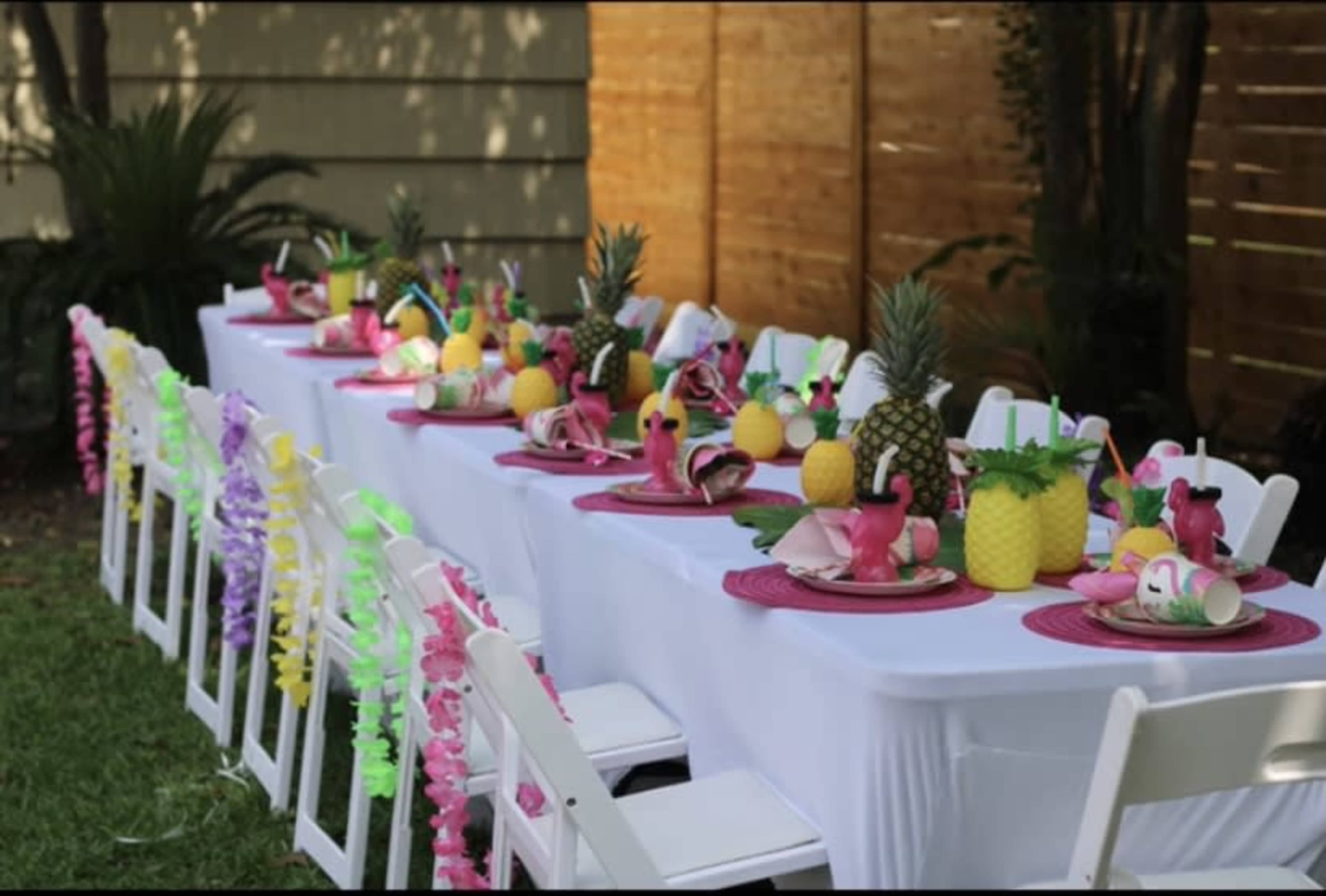 A long outdoor table is set with vibrant plates, tropical decorations, and pineapples for a festive gathering.