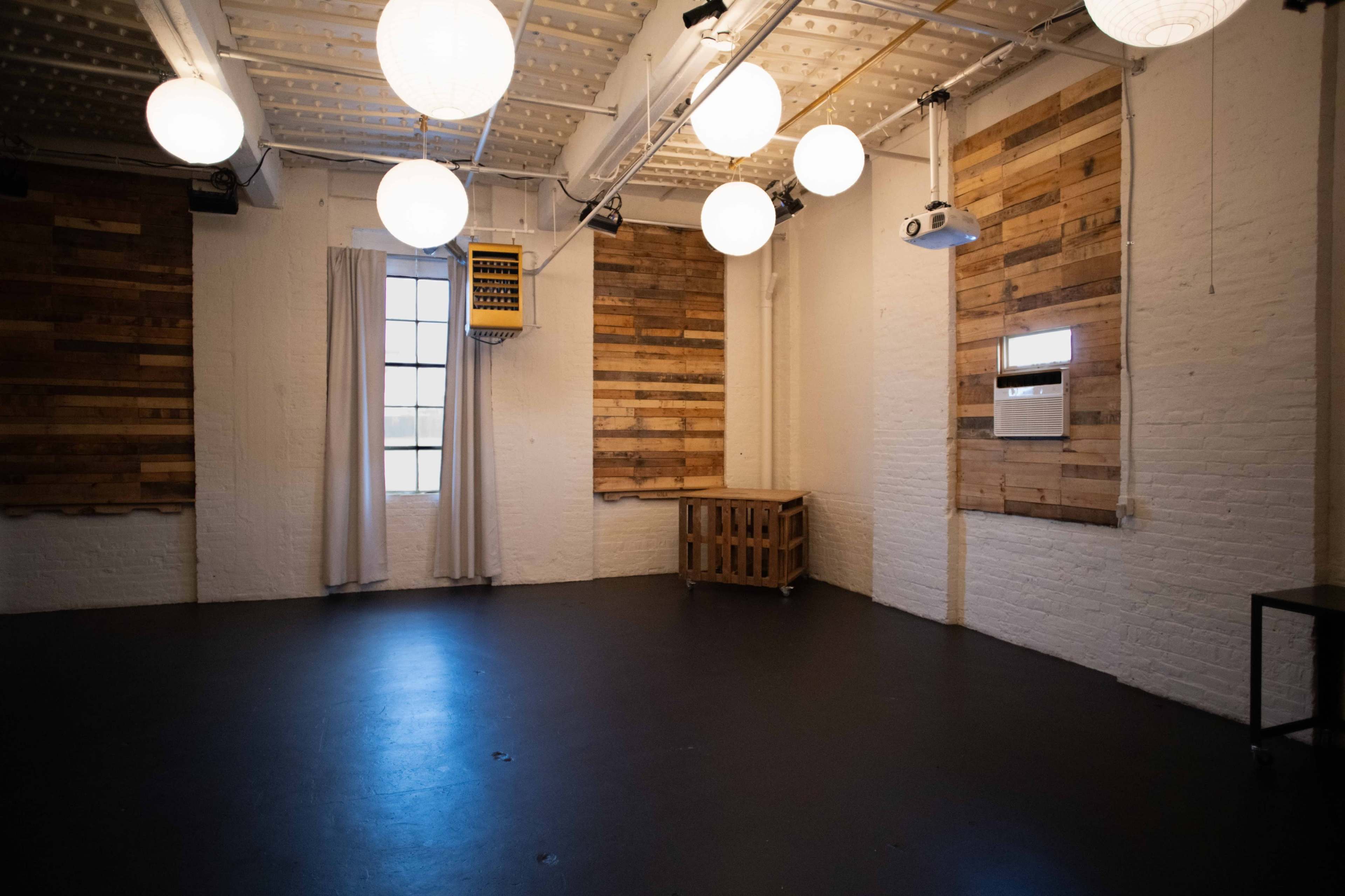The room features white walls, dark flooring, a wooden crate, and overhead spherical lights.