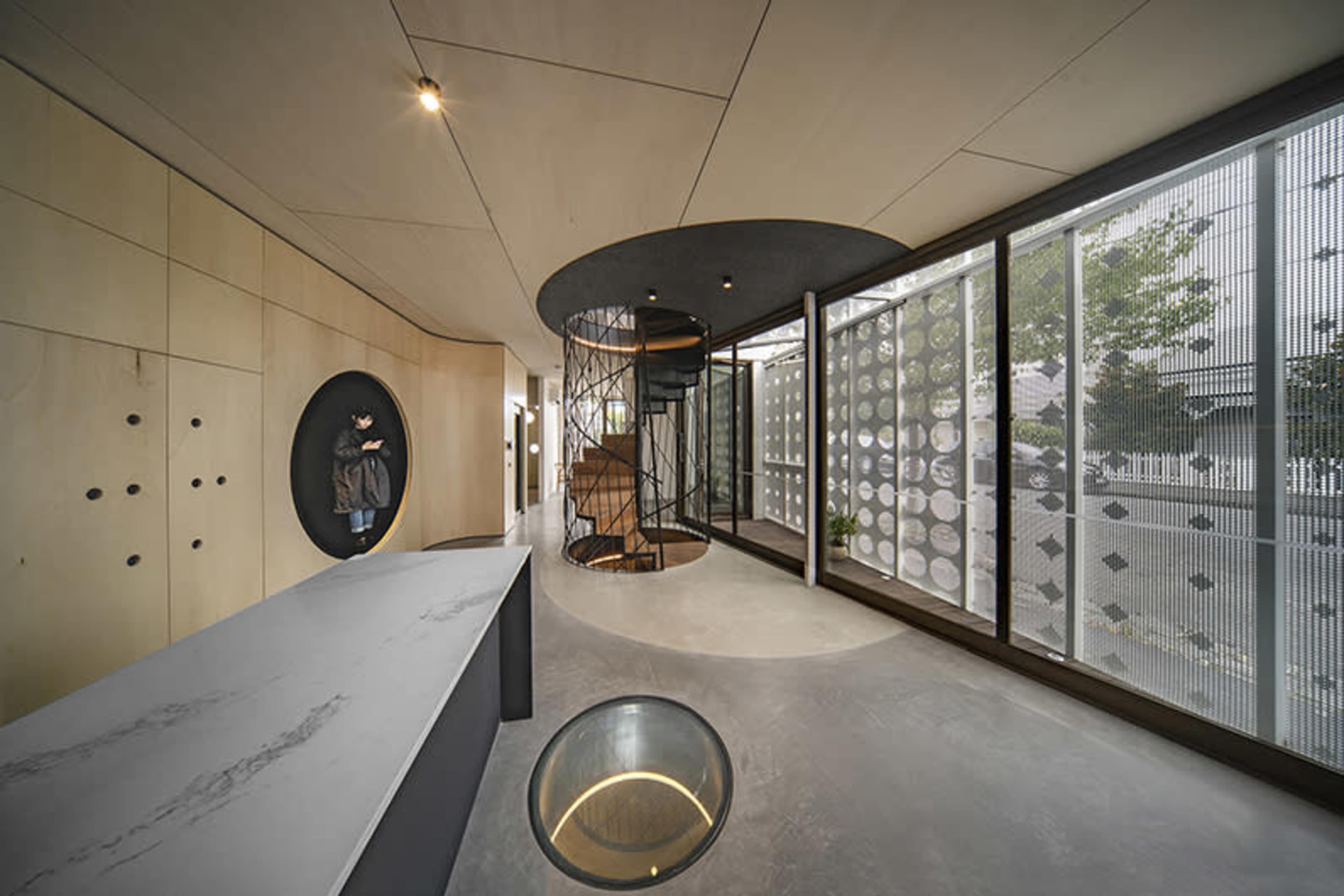 A modern interior space featuring circular design elements, a spiral staircase, and large windows that provide natural light.