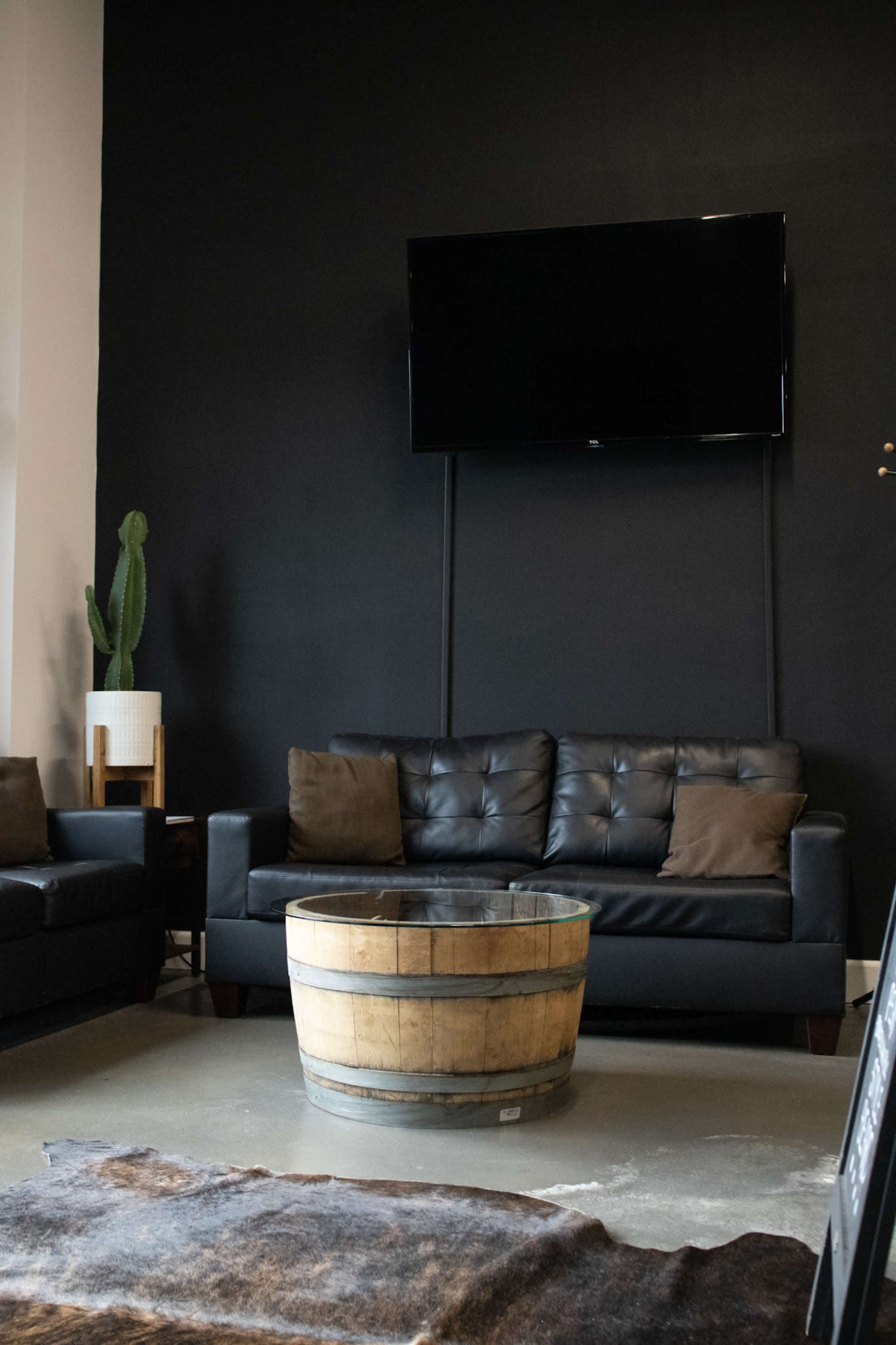 A modern living room with a black wall, a black leather sofa, a round wooden coffee table, and a television mounted above.