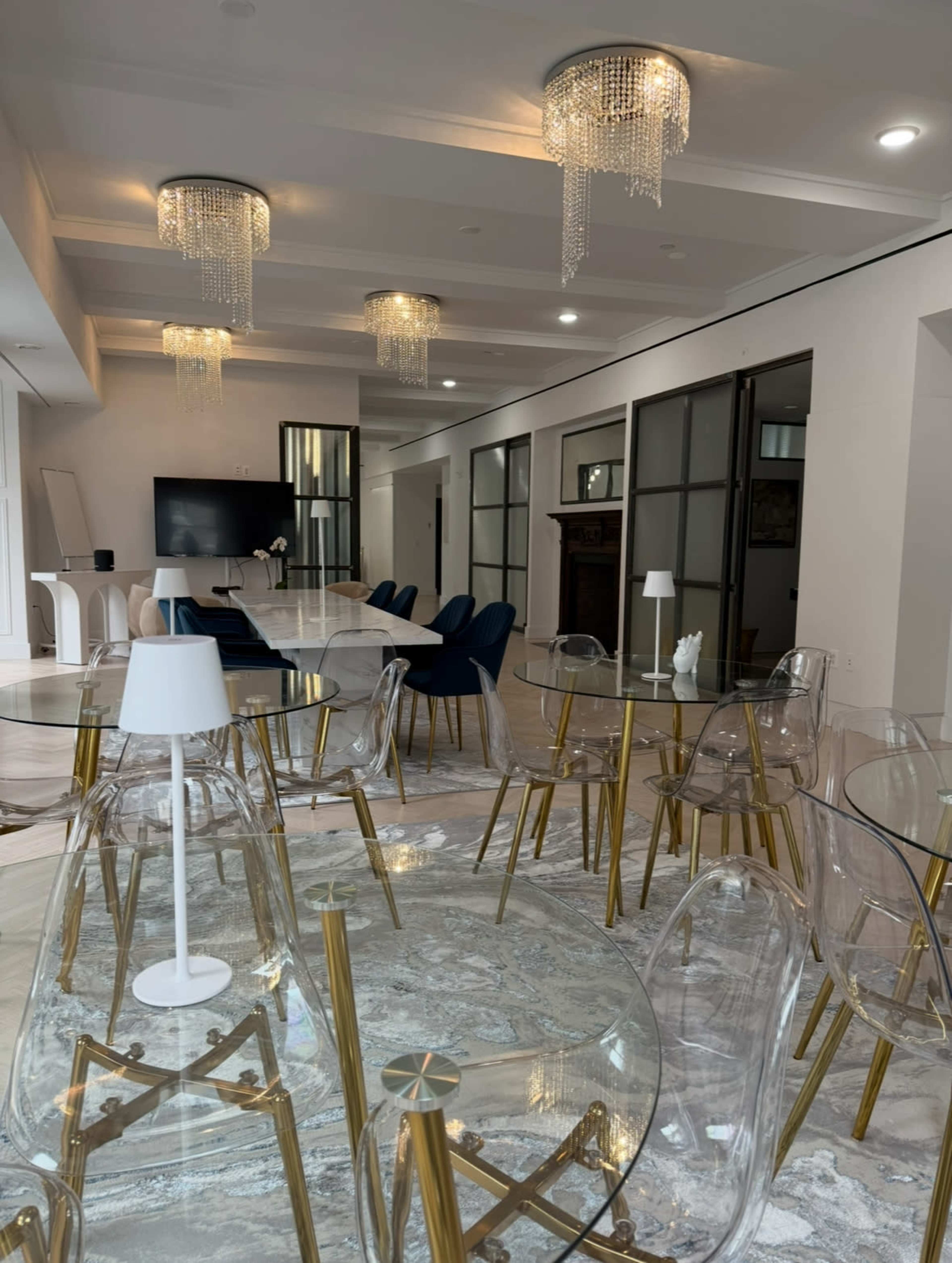 The image shows a modern dining area with transparent chairs, gold accents, and pendant lights hanging from the ceiling.