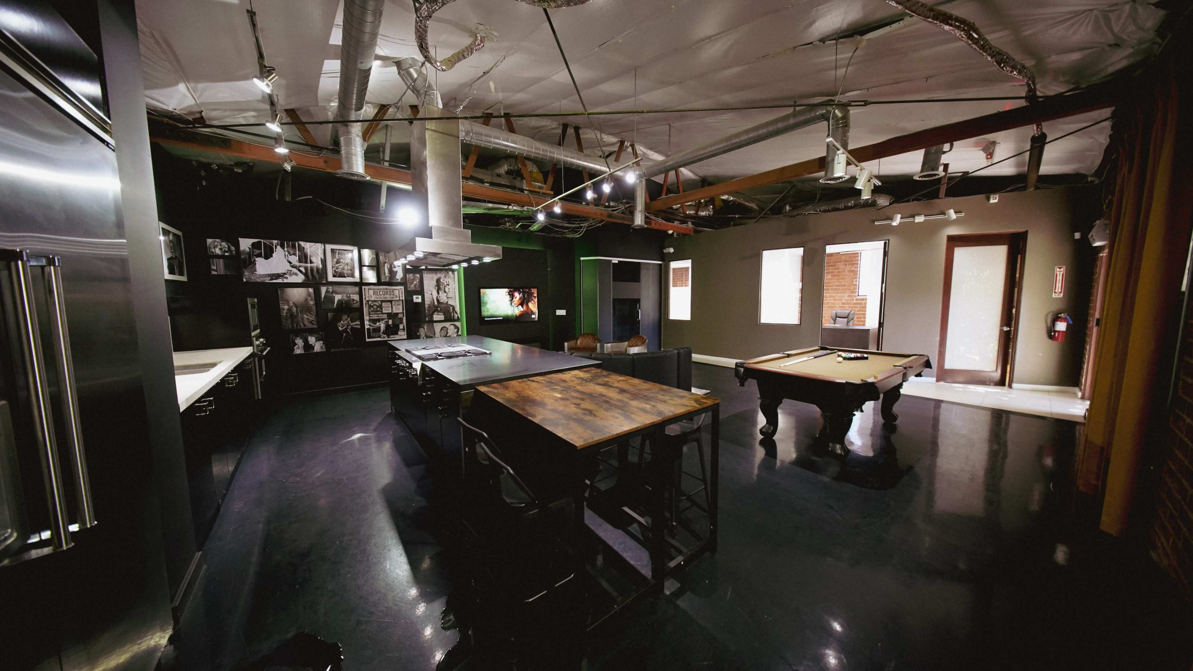 The image shows a spacious, modern room with a pool table, a large dining table, and walls adorned with framed photographs.