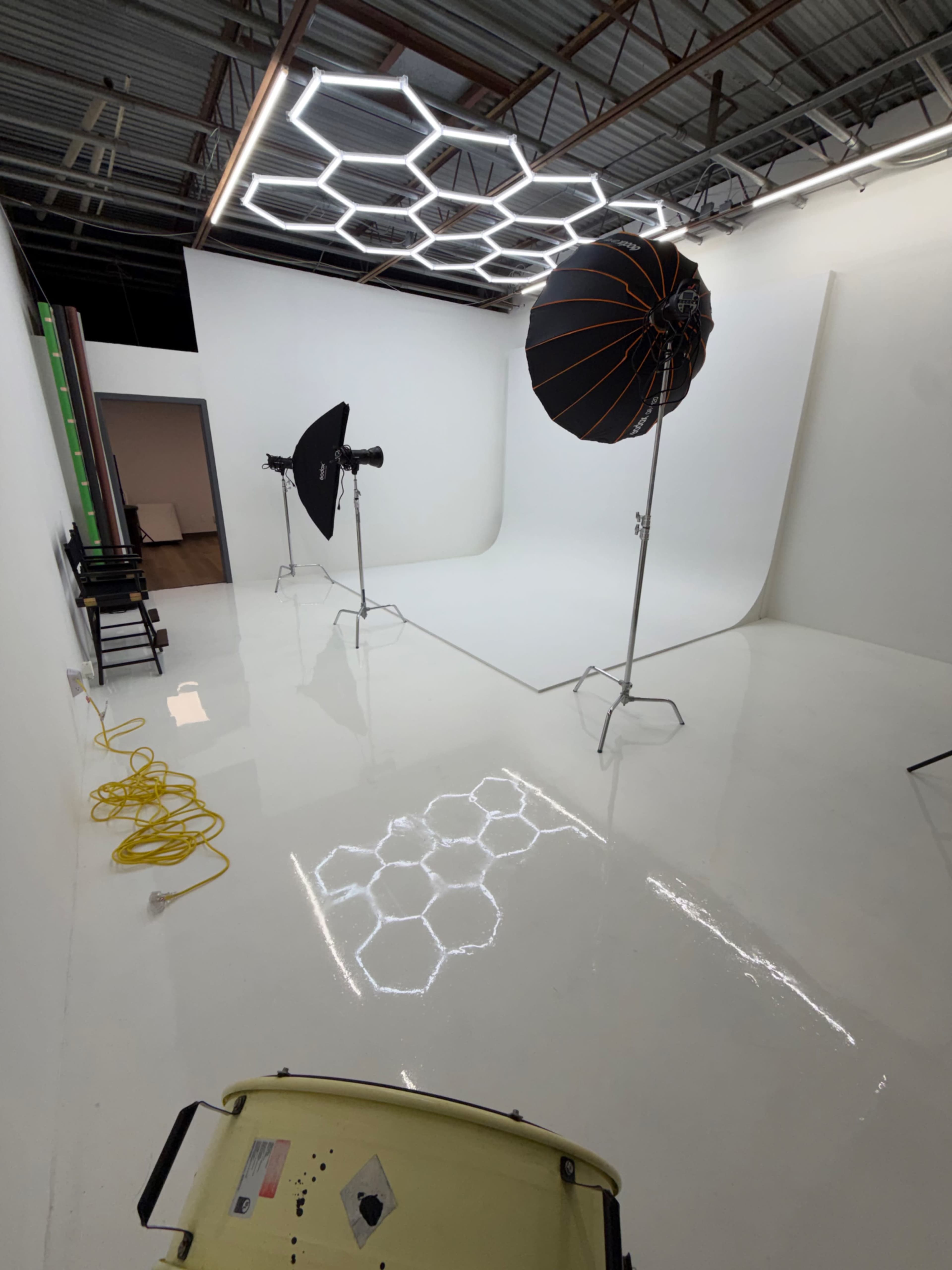 The image shows a photography studio with hexagonal lighting fixtures, two softbox lights on stands, and a clean, reflective white floor.