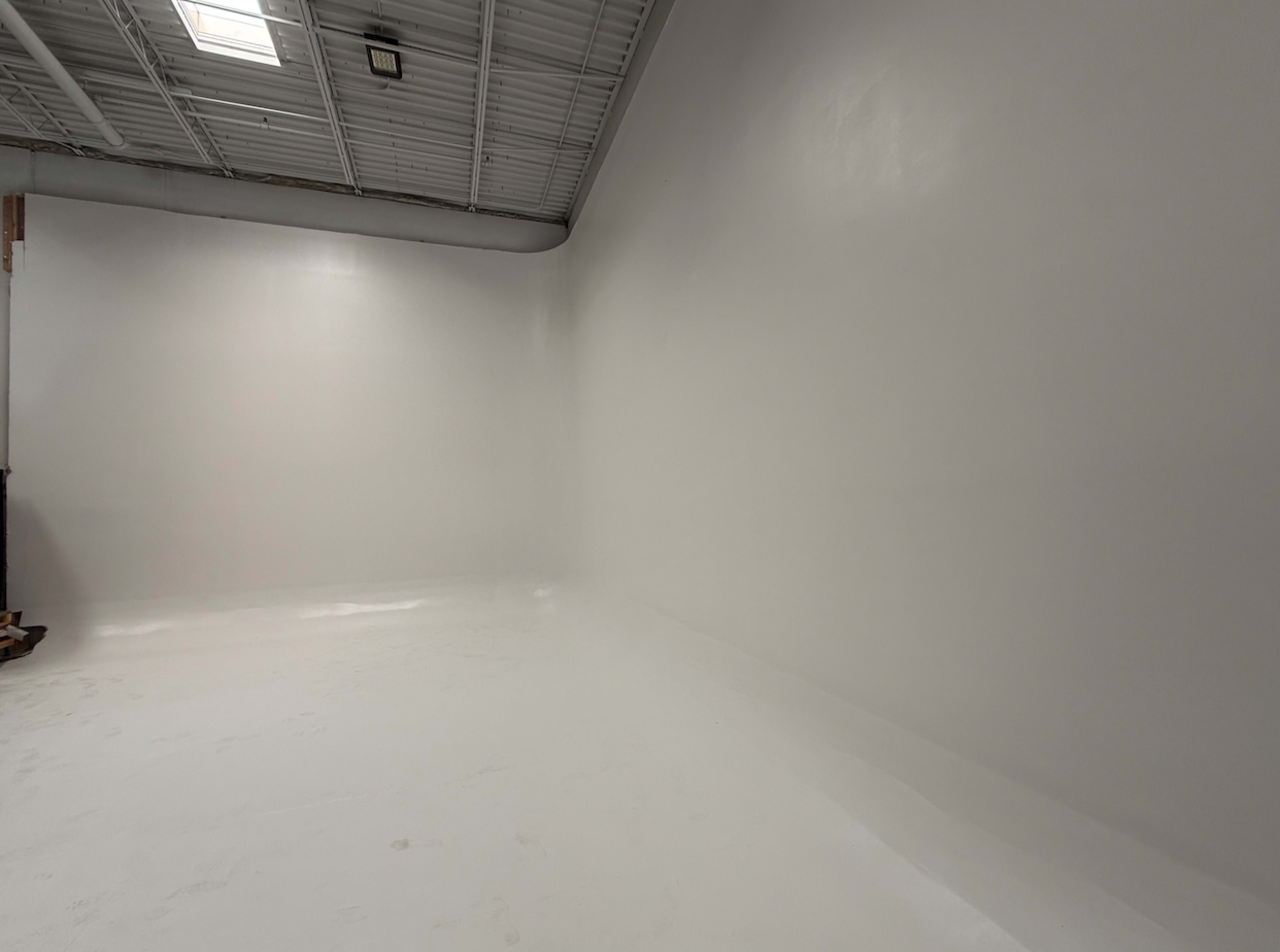 The image shows a blank, white room with smooth walls and a polished floor, illuminated by overhead lights.