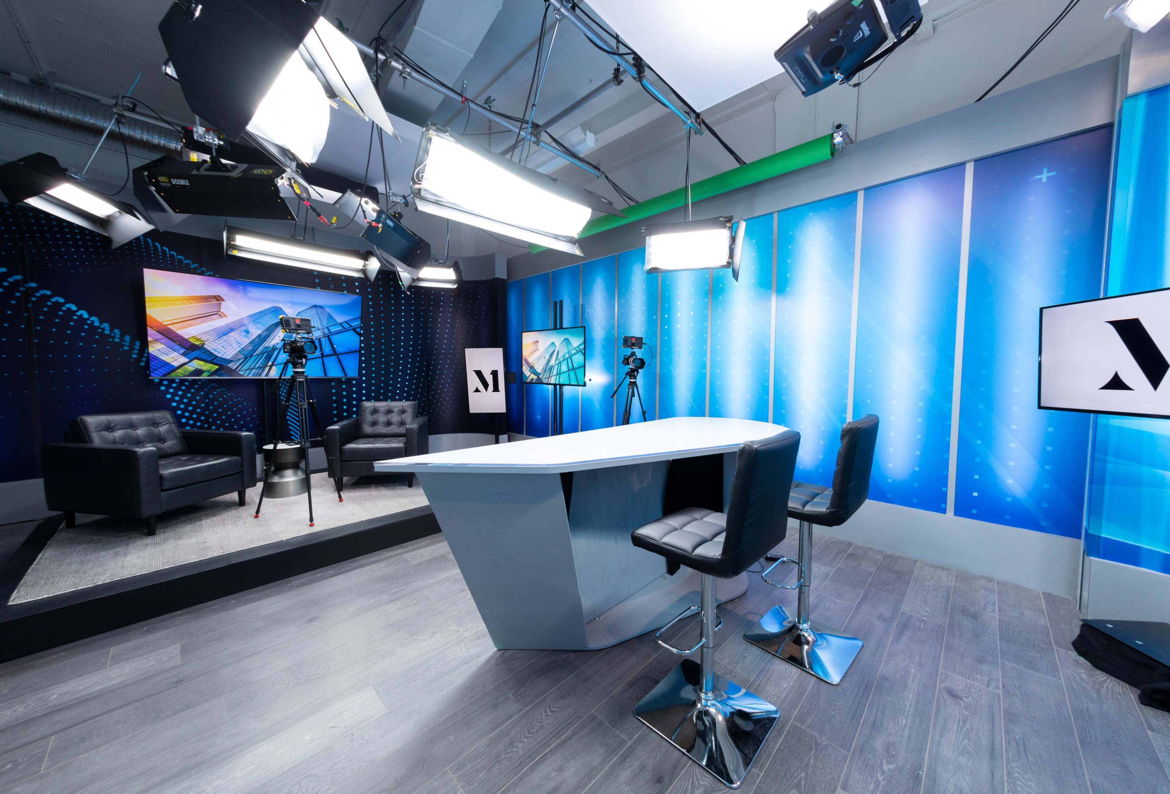 A modern television studio setup with a sleek news desk, cameras, and multi-light rigging against a blue backdrop.