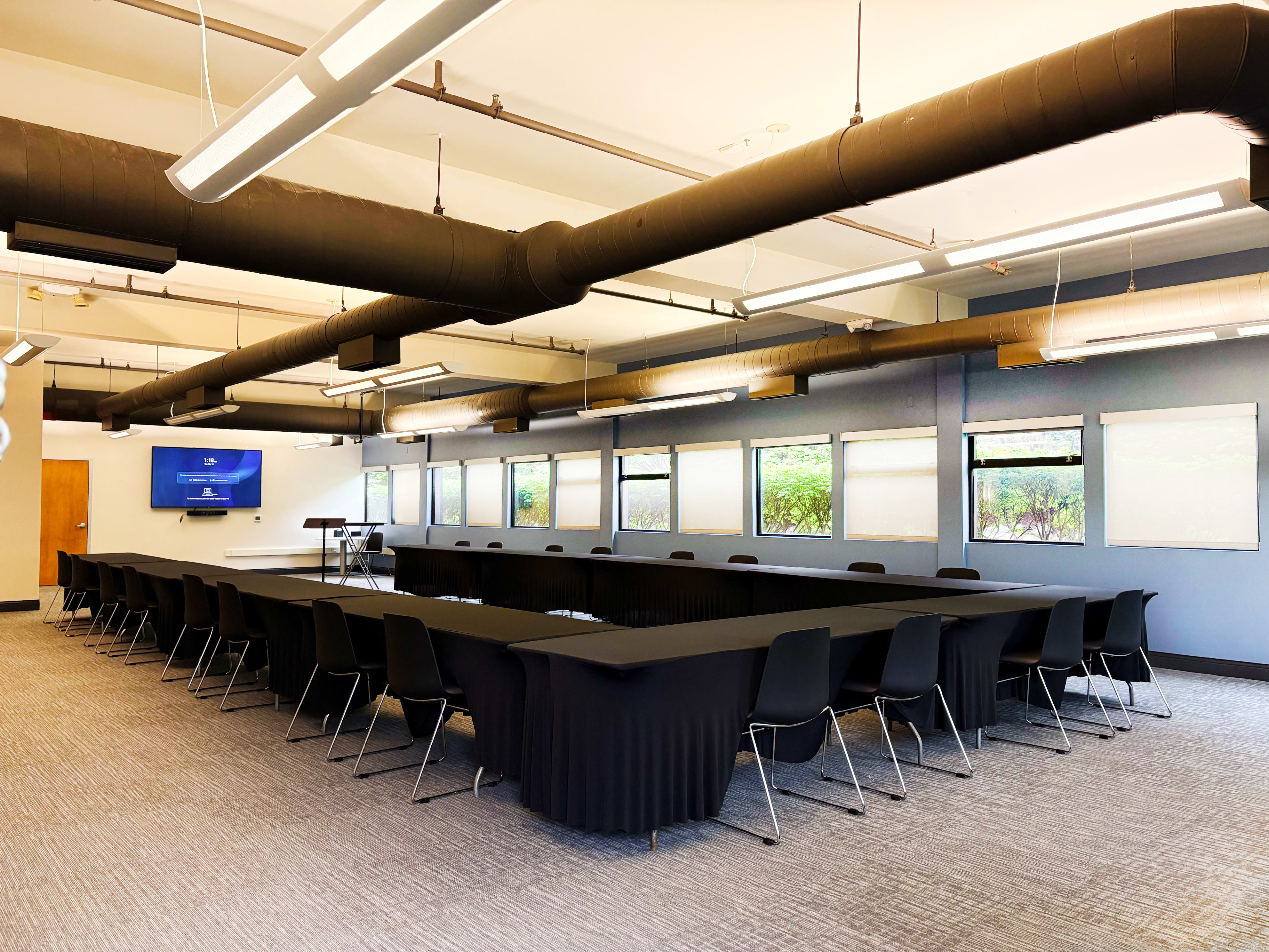 The image shows a conference room with a large rectangular table surrounded by black chairs, and multiple windows allowing natural light.