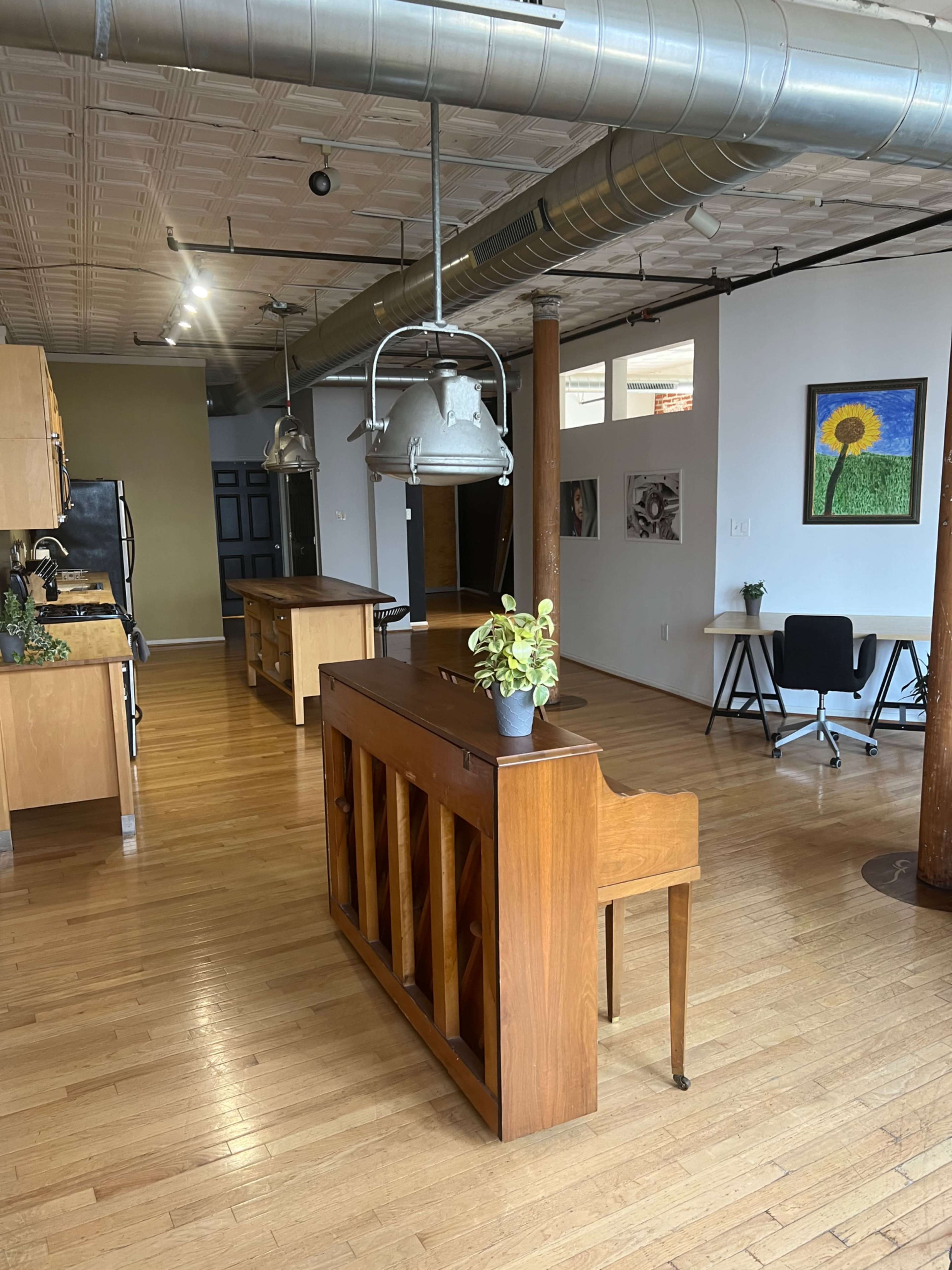 A spacious, modern kitchen and living area featuring hardwood floors, a vintage wooden piano, and various furnishings including a plant and desk.